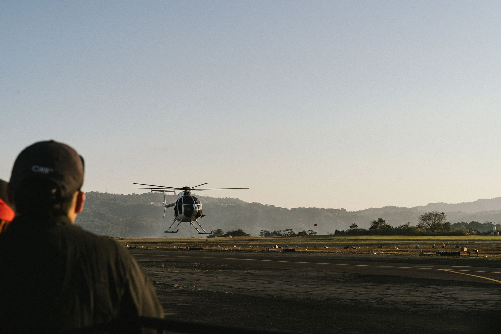 Un helicóptero despega del Aeropuerto de Ilopango en El Salvador, con montañas al fondo.