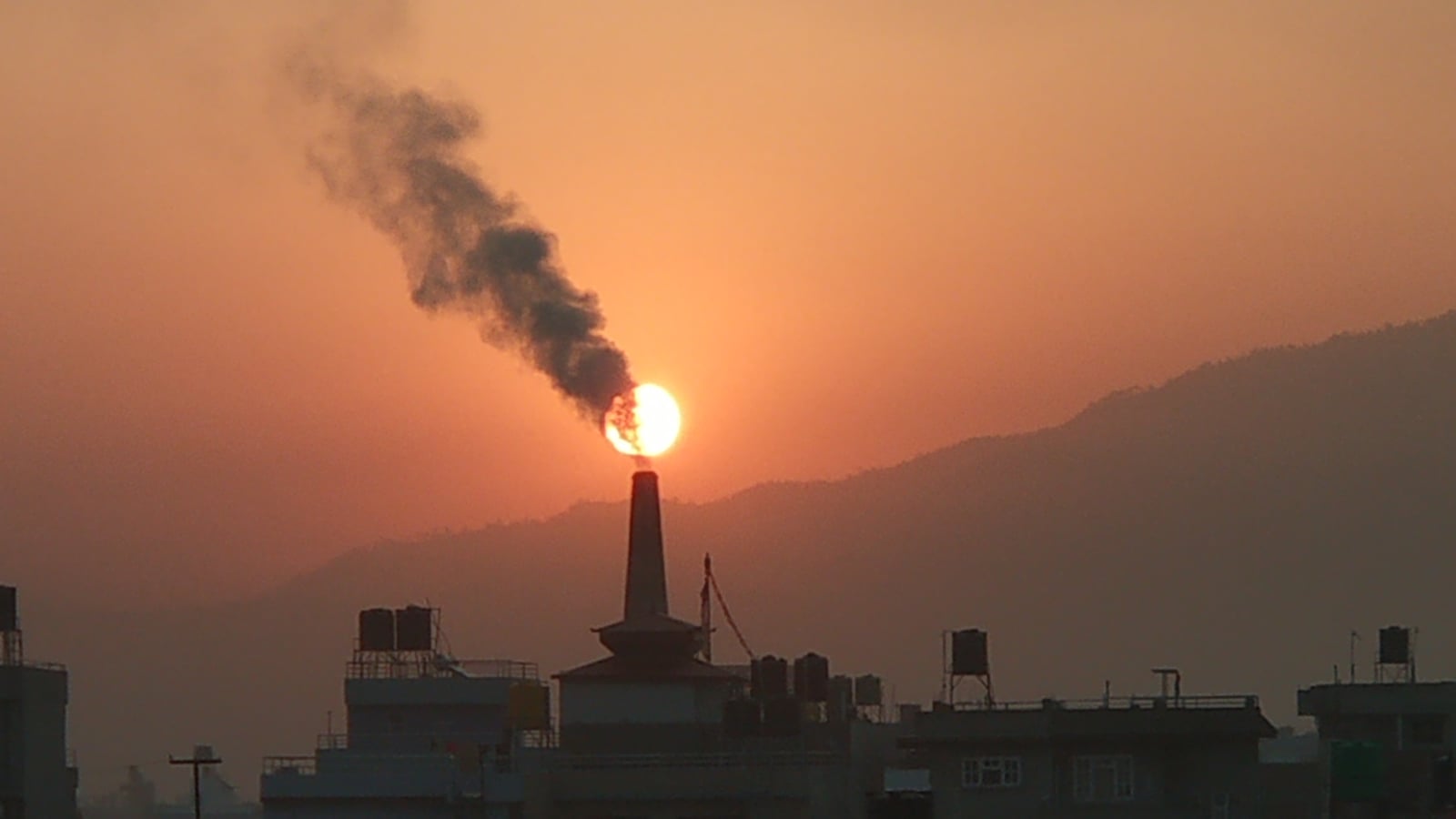 Air pollution by brick factories. The sun can be seen in the background just above the factory chimney, partially covered by the chimney's smoke.
