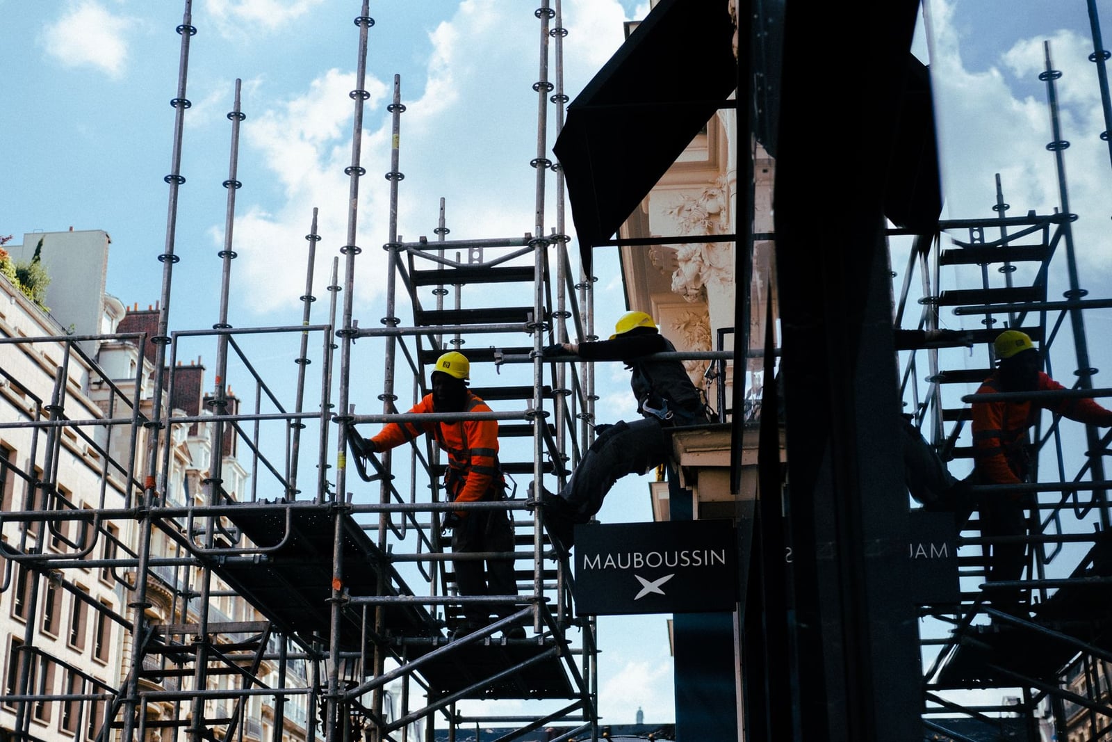 Trabajadores de la construcción silueteados en andamios en un entorno urbano bajo cielos azules.