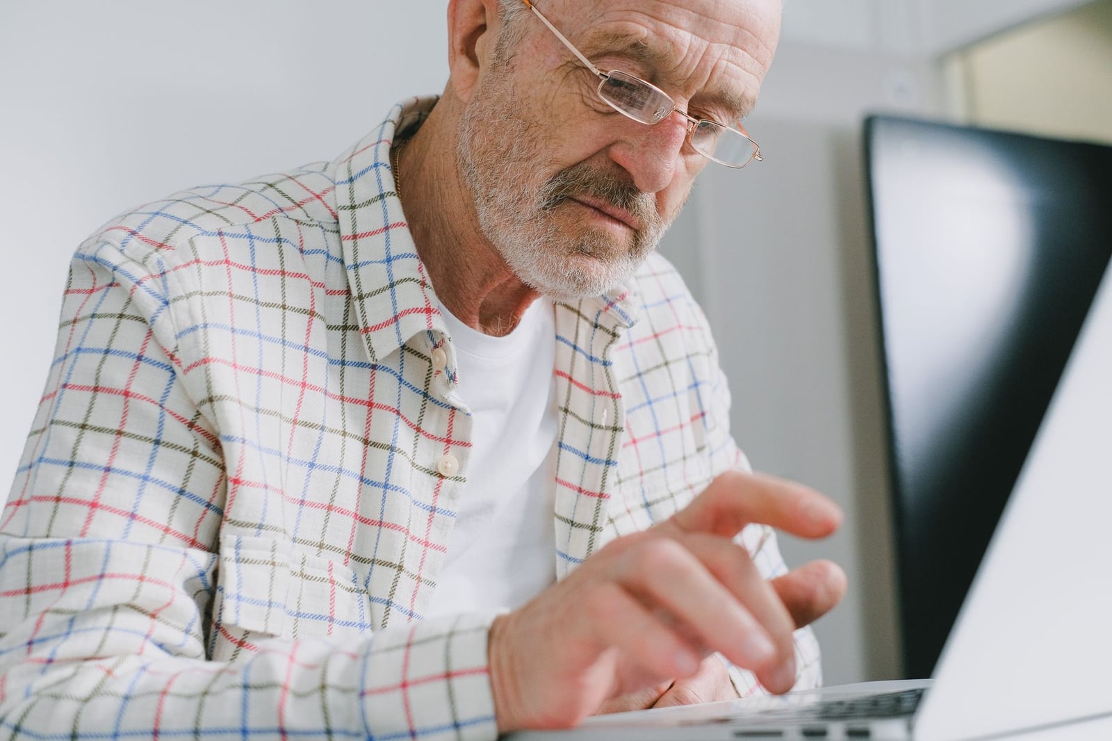 Hombre anciano con camisa de cuadros usando un portátil en interiores.