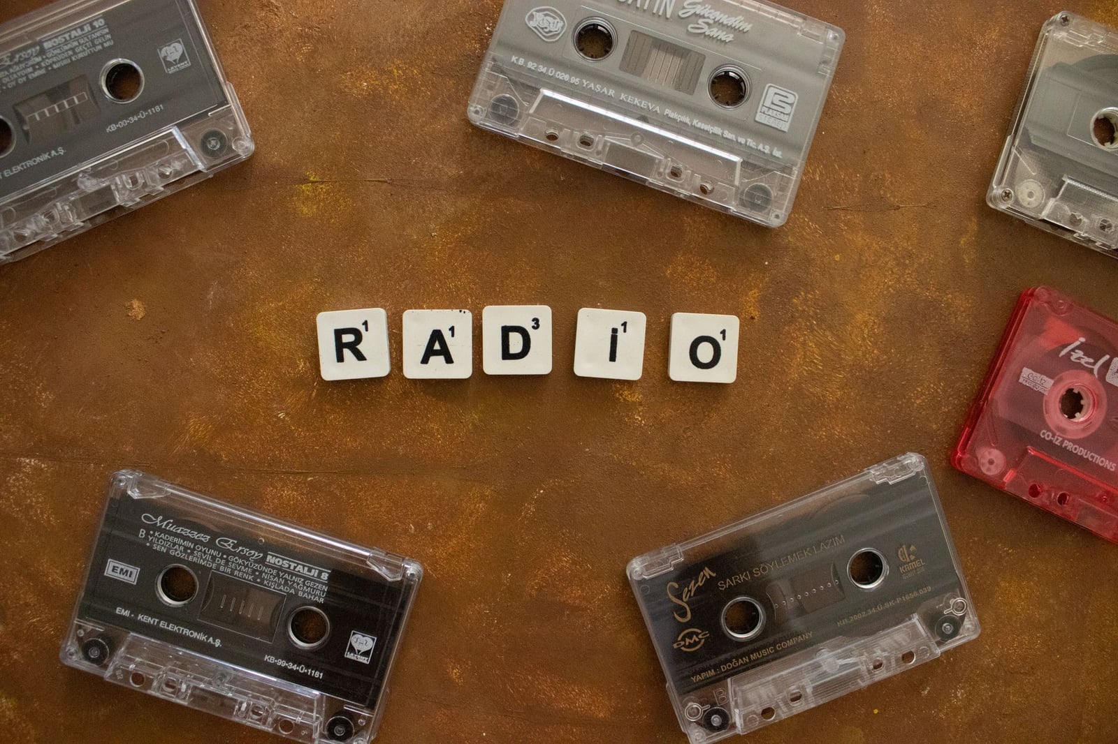 Cintas de casete retro dispuestas alrededor de fichas de Scrabble que forman la palabra "RADIO" sobre un fondo rústico.