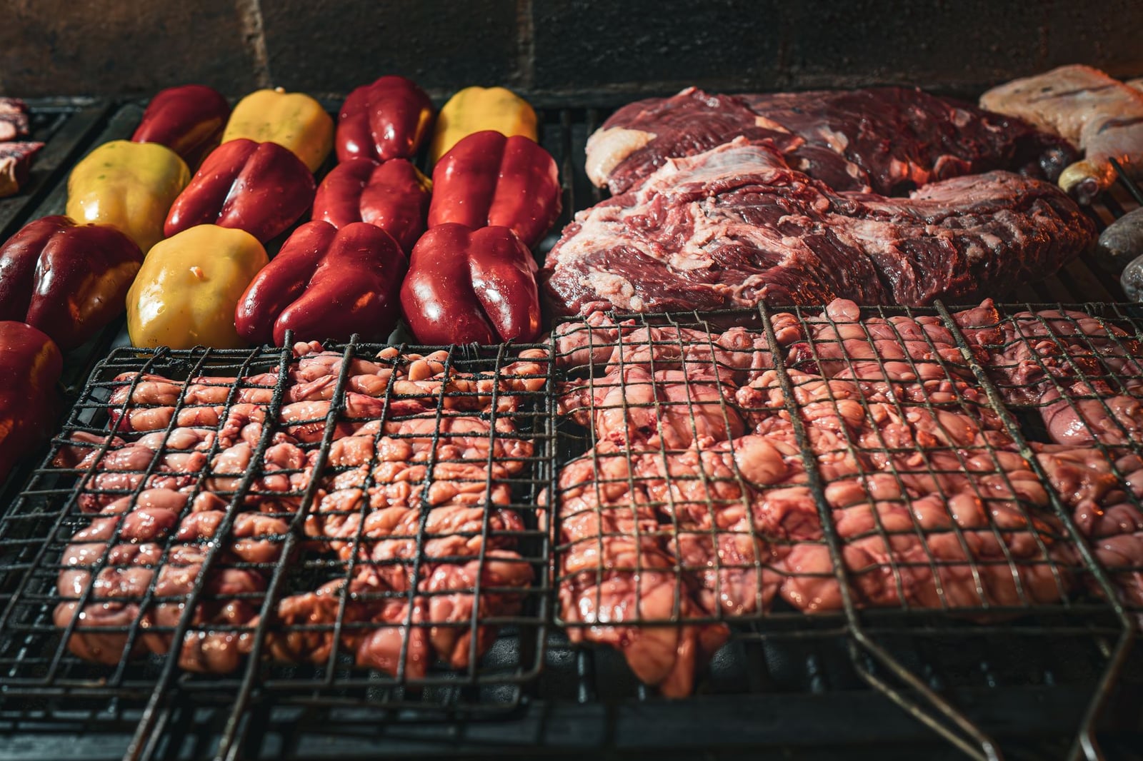 Carnes y pimientos variados siendo asados sobre carbón, capturando una experiencia rústica de barbacoa.