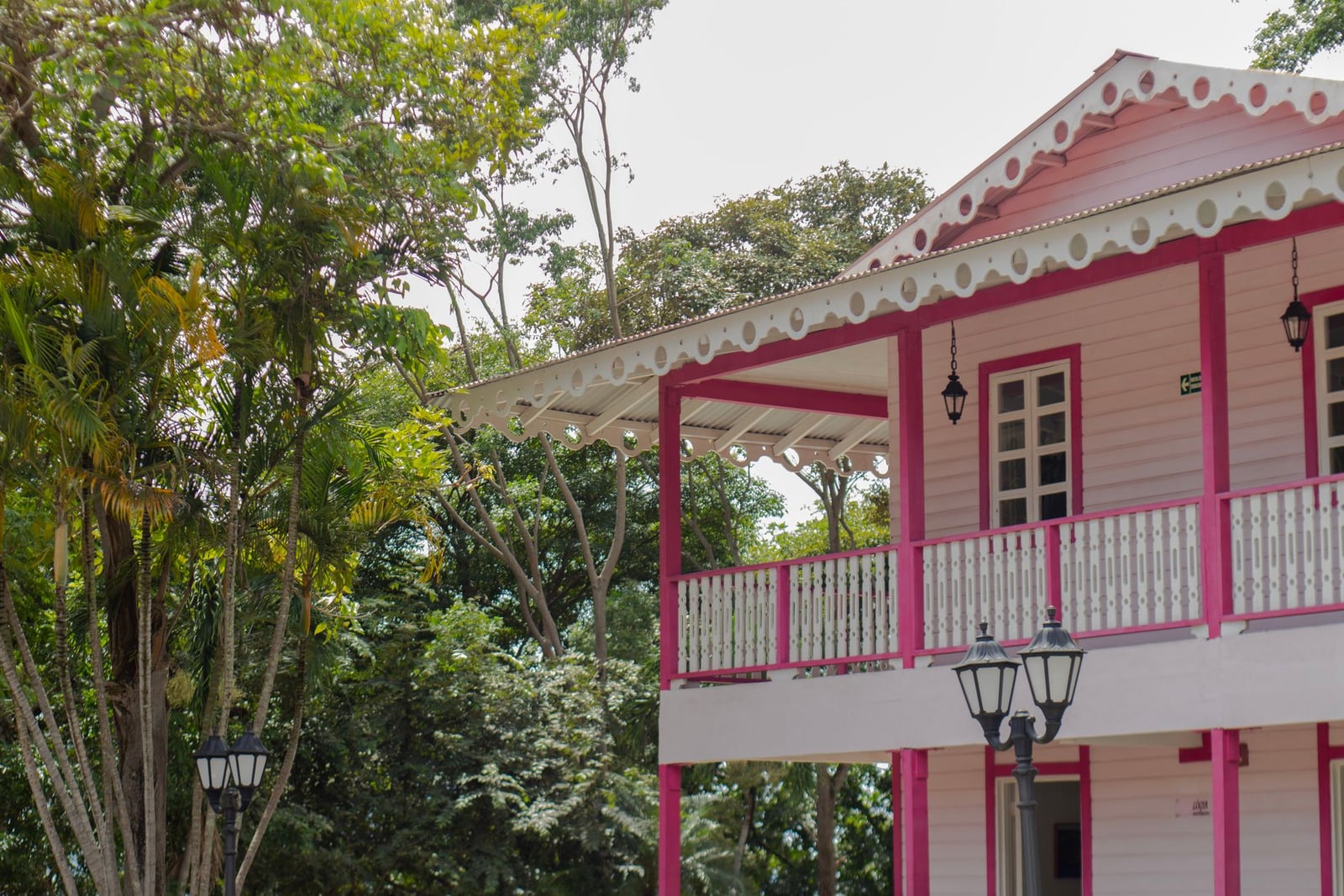 Una pintoresca casa de madera rosa y blanca con detalles ornamentales en medio del follaje verde, capturando una escena al aire libre serena.