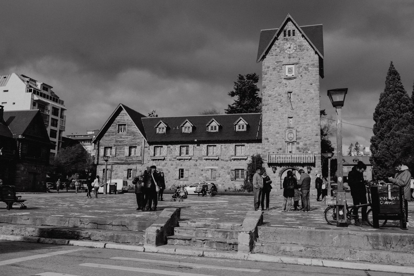 Foto en blanco y negro de un edificio histórico de piedra con torre del reloj y personas en un día nublado.