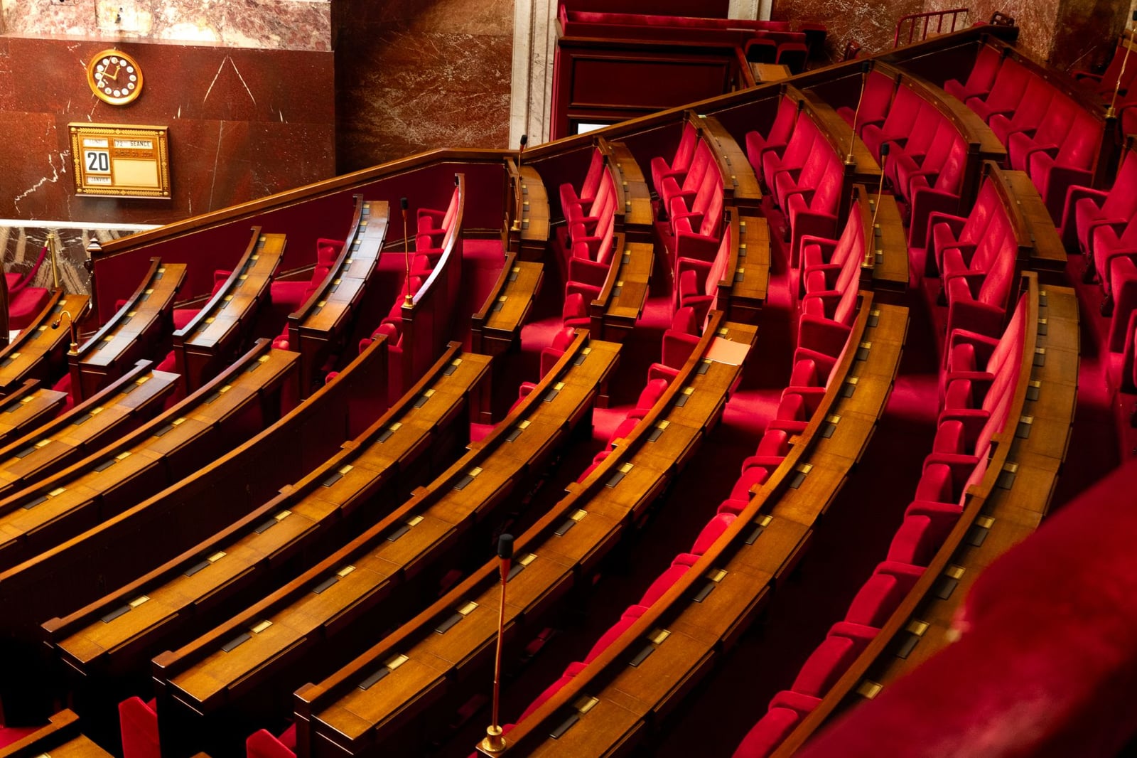 Una lujosa vista interior de una cámara legislativa con asientos rojos curvos y escritorios de madera.