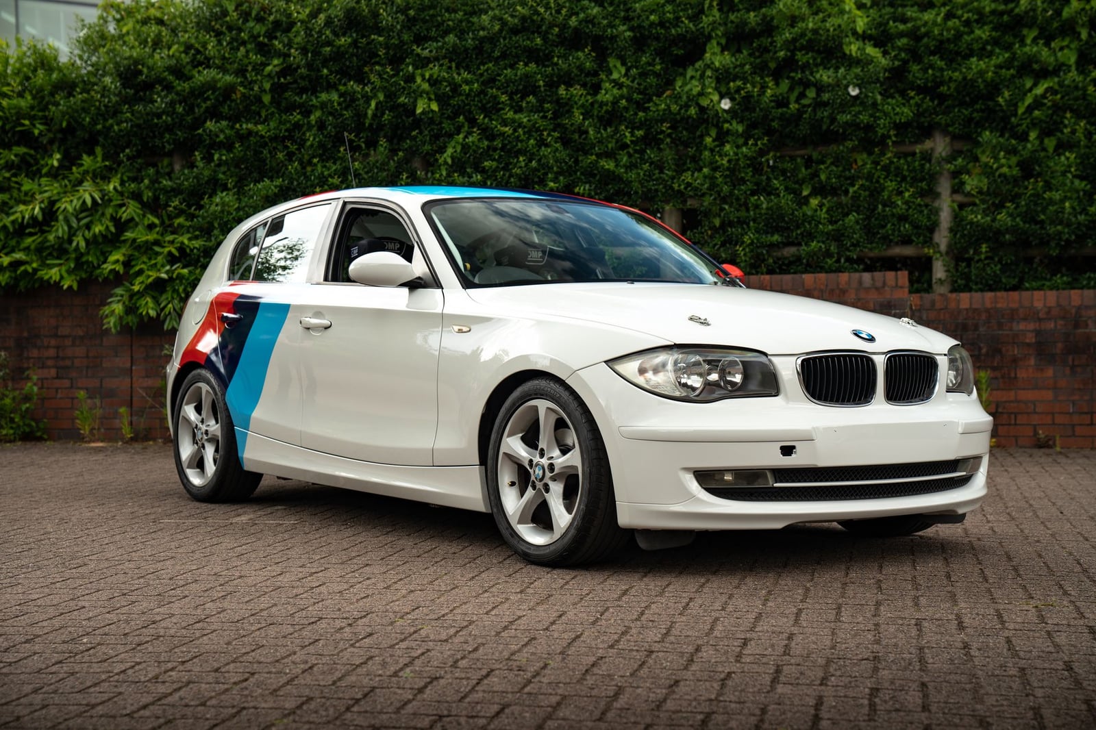 BMW blanco con rayas de colores estacionado sobre una acera de ladrillos en Southampton, Inglaterra.