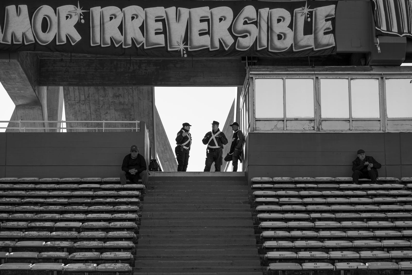 Foto en blanco y negro de una grada de estadio en Córdoba, Argentina, con presencia policial.