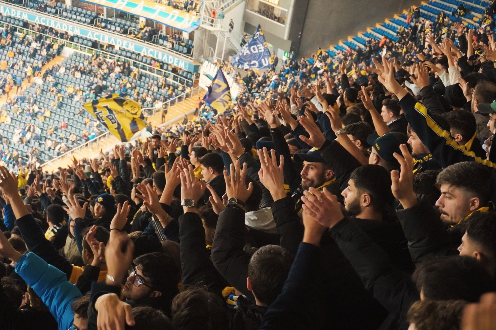 Aficionados enérgicos con las manos levantadas en un estadio, apoyando a su equipo de fútbol con entusiasmo.