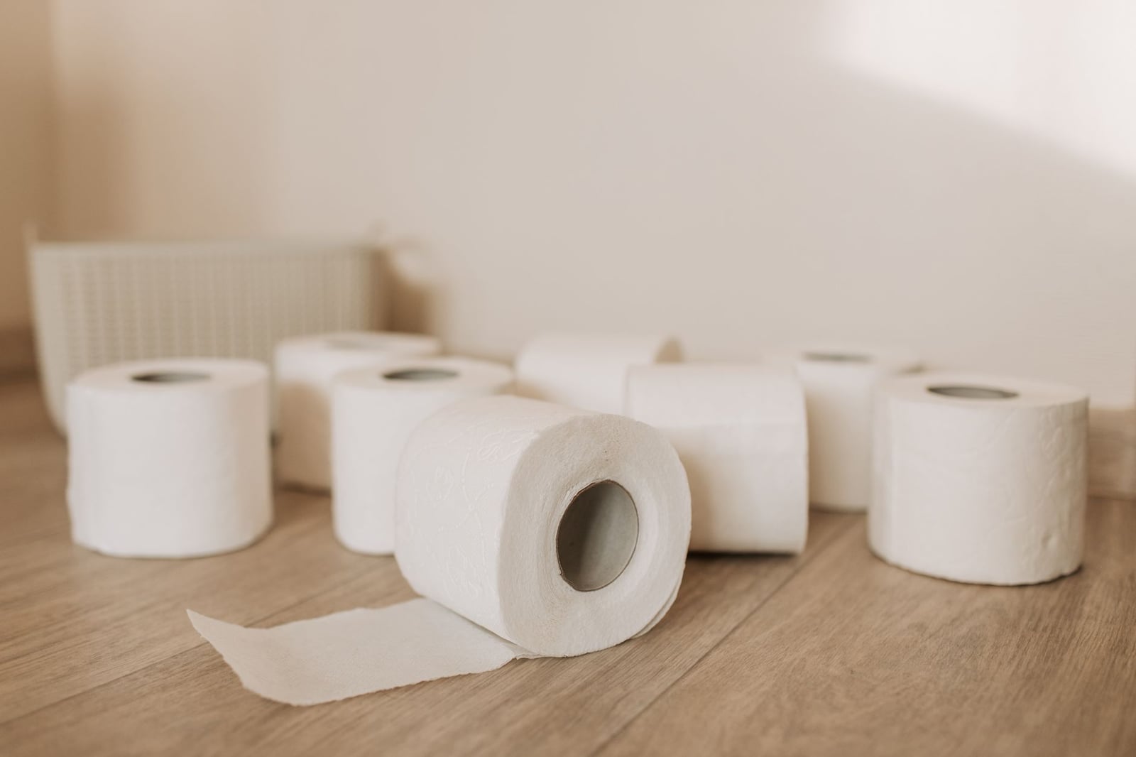 Una colección de rollos de papel higiénico esparcidos sobre un suelo de madera con luz suave, representando esenciales cotidianos.