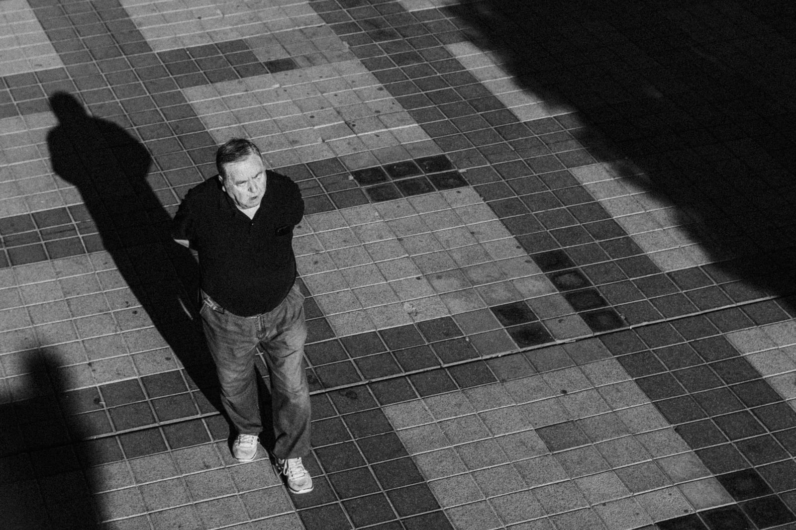 Un hombre mayor camina por una calle adoquinada en sombra en Madrid, España, enfatizando patrones y contraste de luz.
