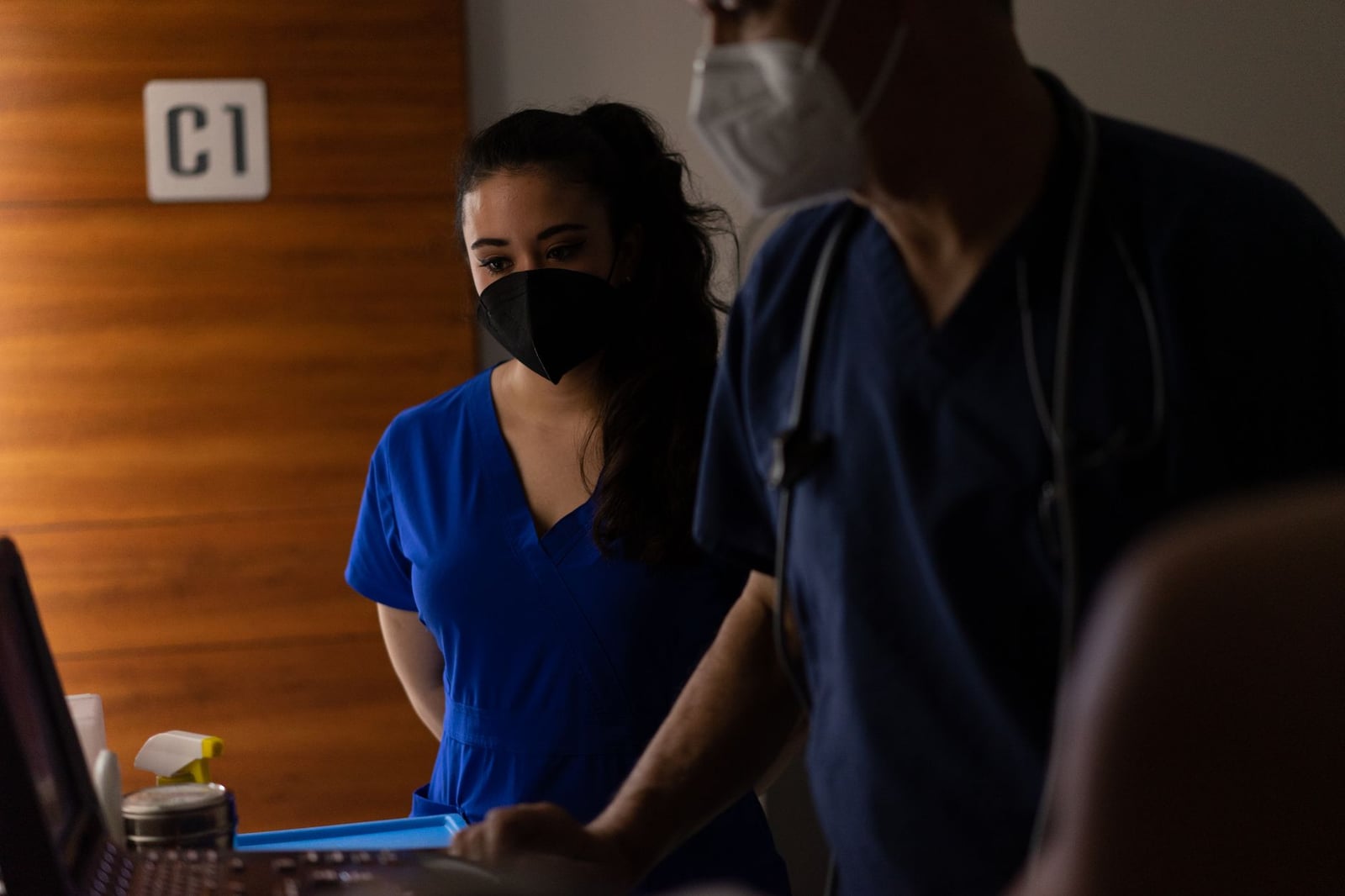 Médicos en batas y mascarillas examinando datos de pacientes en una sala de hospital.