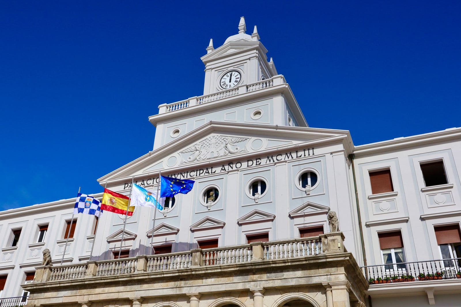 Vista en ángulo bajo del Palacio Municipal con banderas en Ferrol, España en un día soleado.