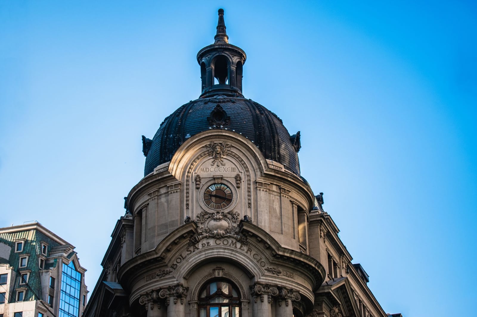 Vista en ángulo bajo de la icónica cúpula del edificio de la Bolsa de Santiago contra un cielo azul claro.