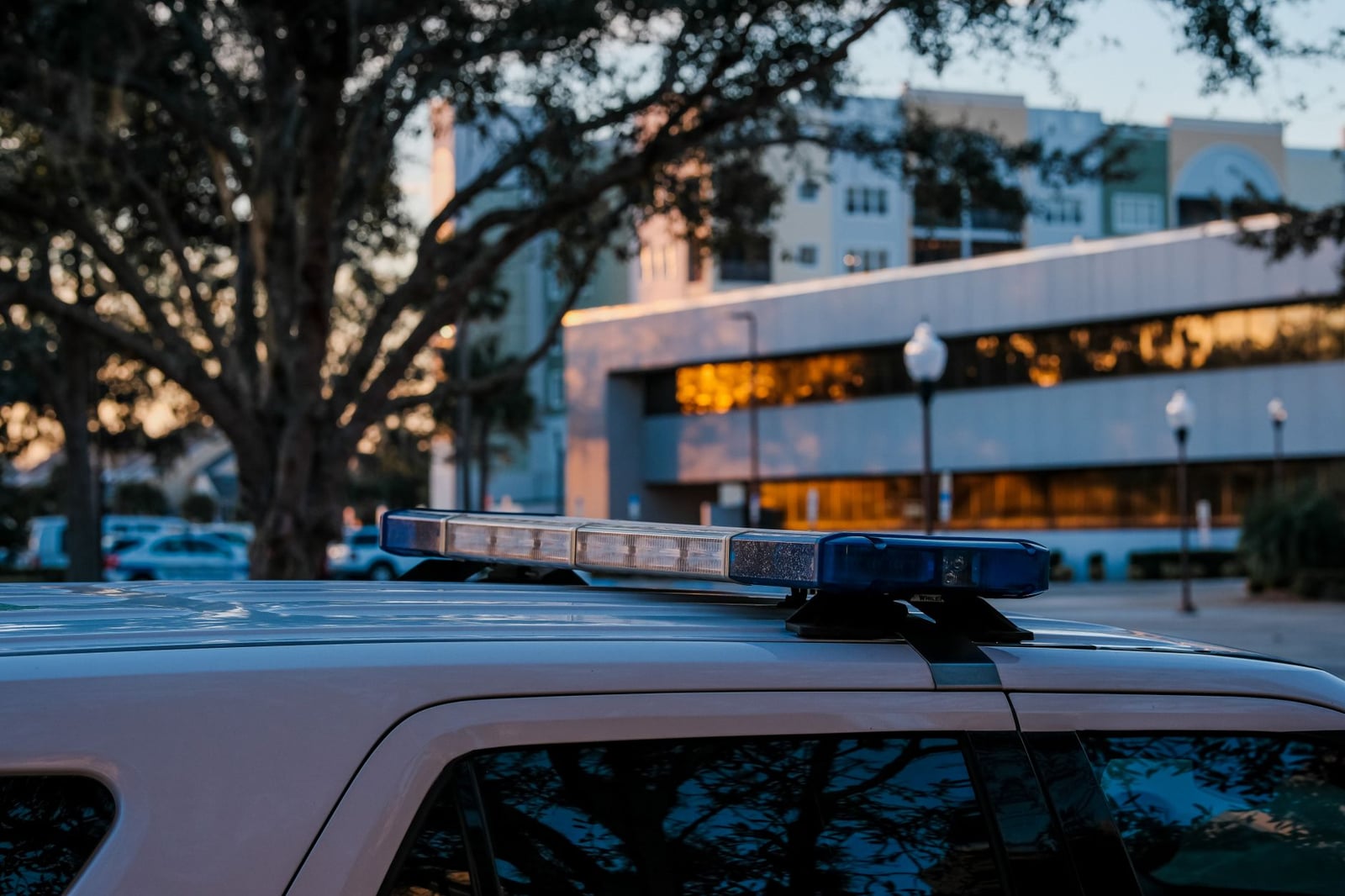 Primer plano de vehículo policial con luces de emergencia frente a edificios urbanos al anochecer.
