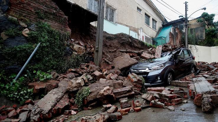 flooded street in northern Chile desert region with damaged buildings, mud and debris, emergency workers in background, overcast sky