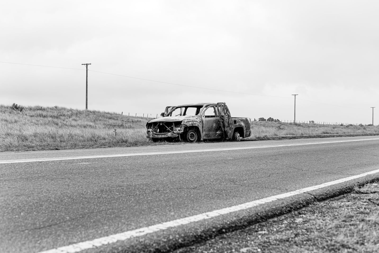 Foto en blanco y negro de un camión oxidado y abandonado en una carretera rural vacía en Buenos Aires.