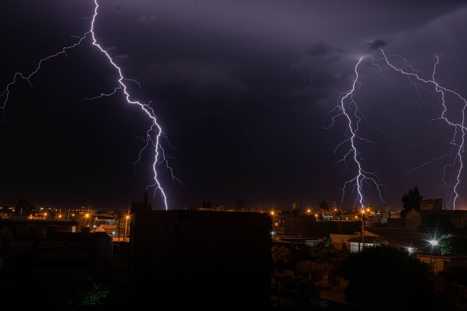 Intensos rayos iluminan una ciudad durante una tormenta nocturna, mostrando el poder de la naturaleza.