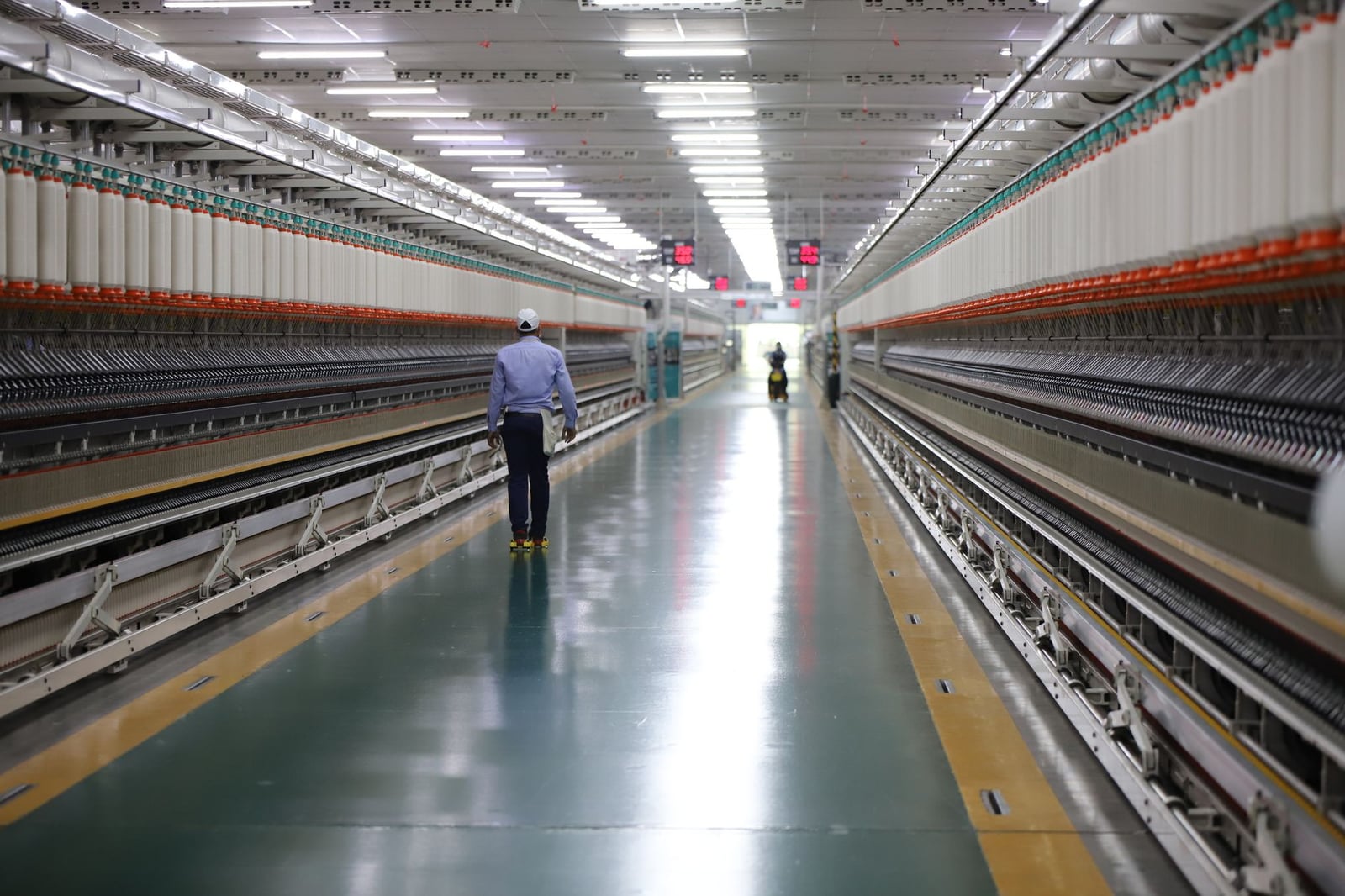 Un hombre camina por un pasillo bien iluminado en una moderna planta textil en India.