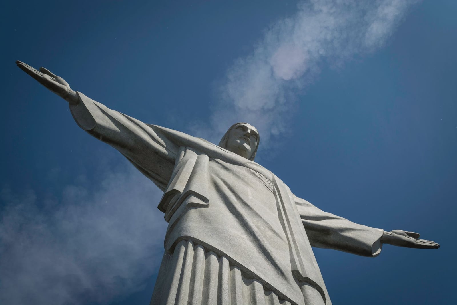 Vista en primer plano de la estatua del Cristo Redentor con los brazos abiertos, contra un cielo azul claro.