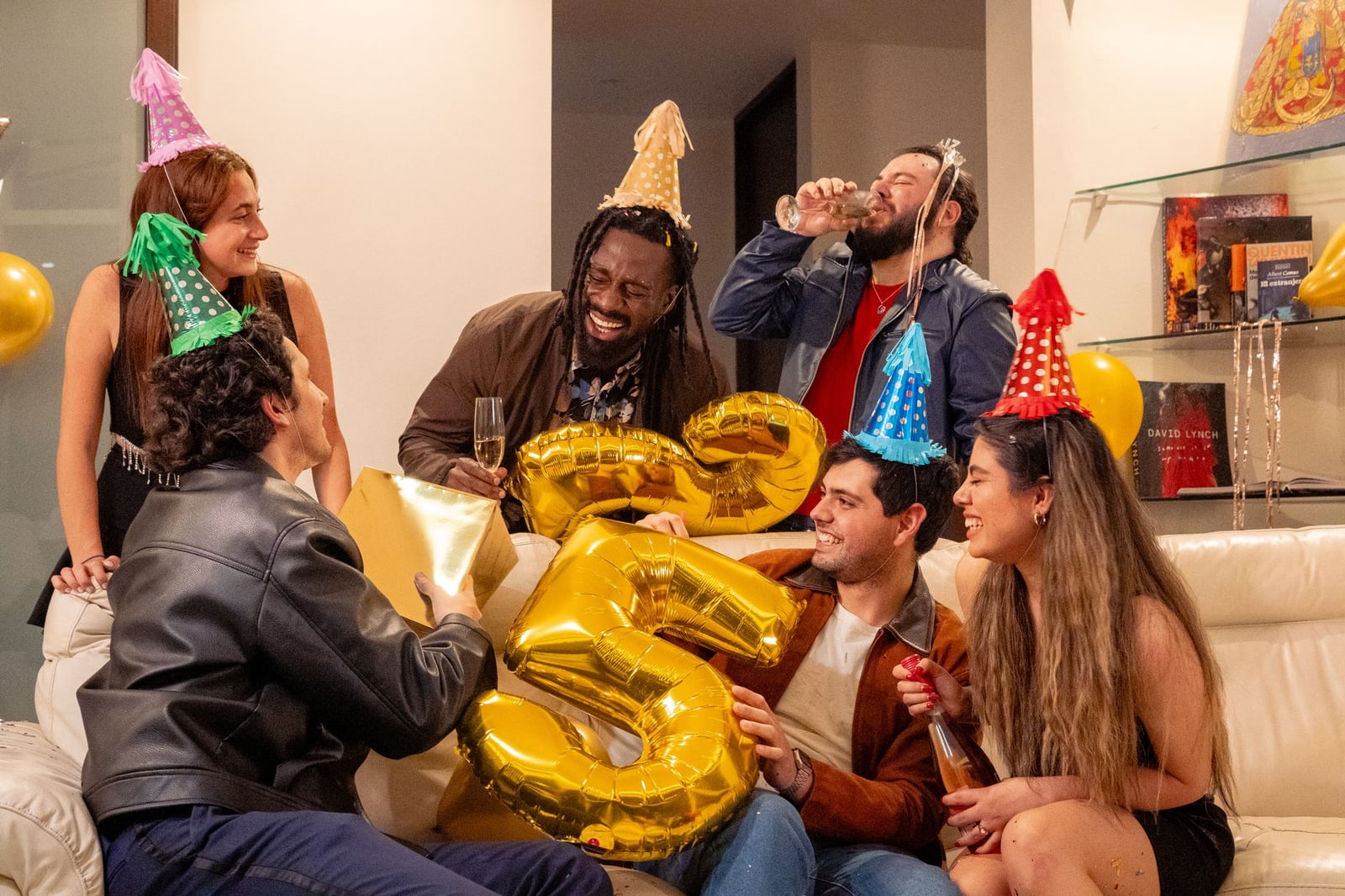 Grupo feliz de amigos celebrando un cumpleaños con globos y gorros de fiesta.
