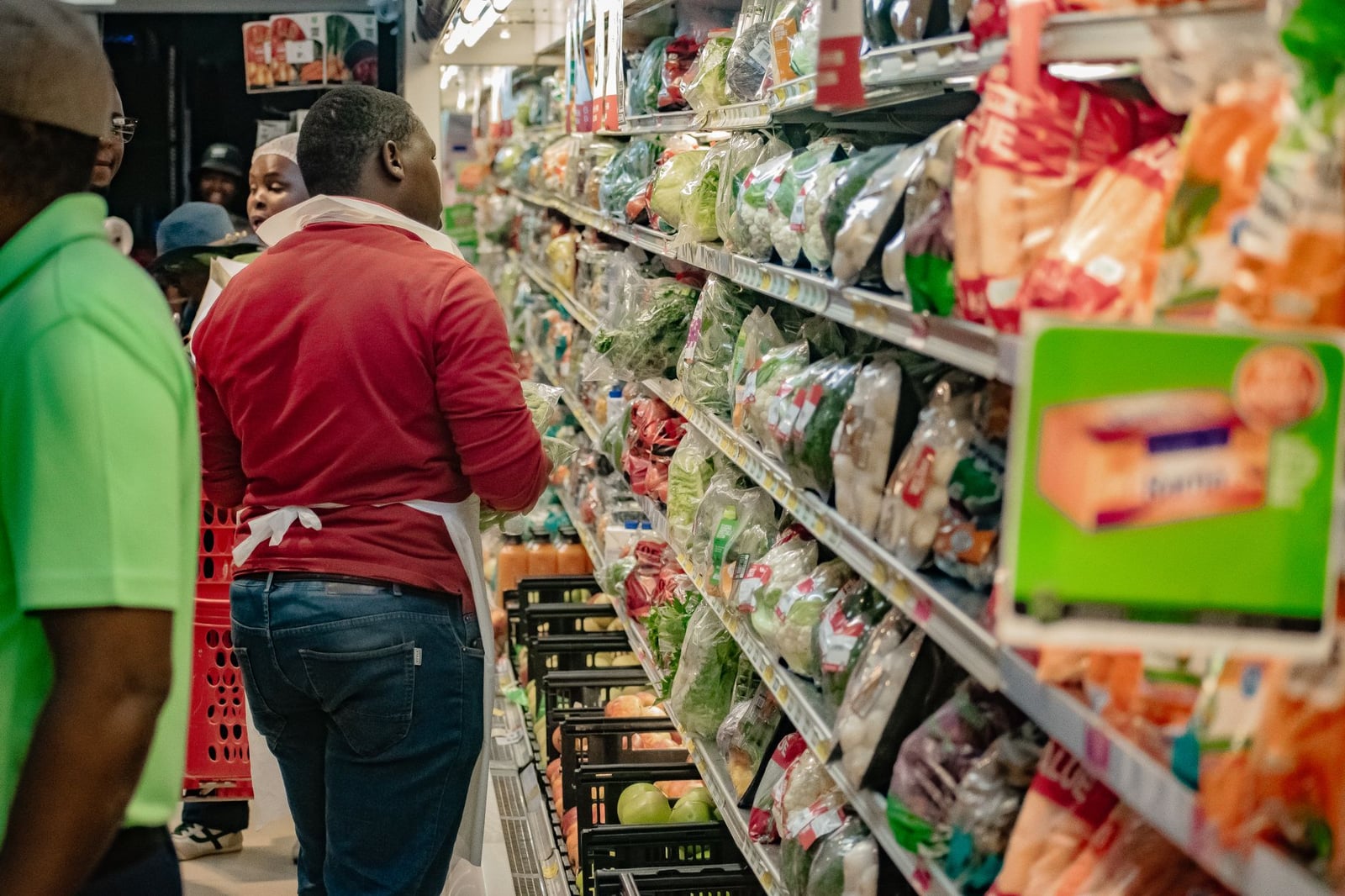 Clientes examinando productos frescos en un pasillo concurrido de un supermercado.