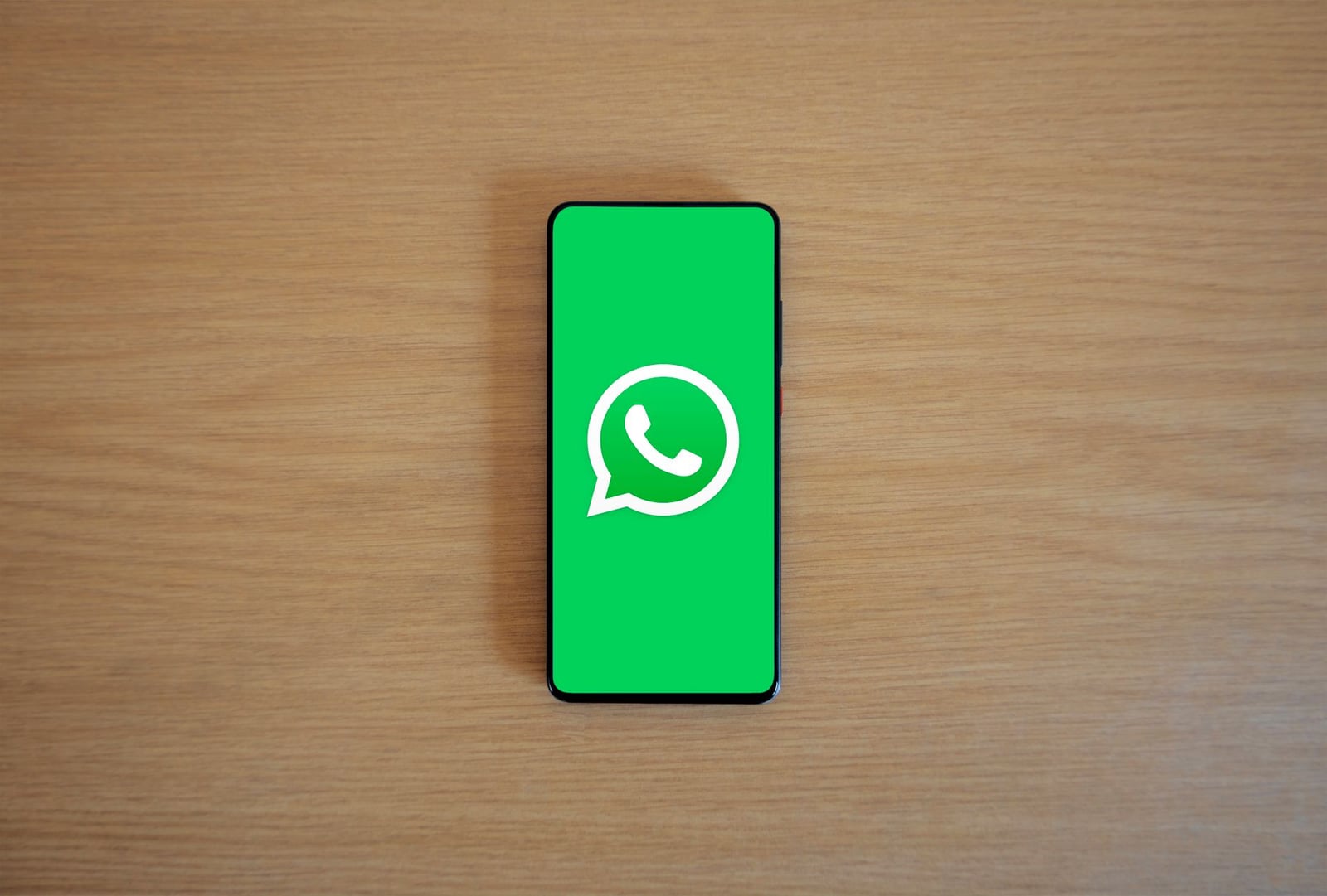 Vista superior de un smartphone que muestra el logo de WhatsApp sobre un fondo de madera, representando tecnología y comunicación.