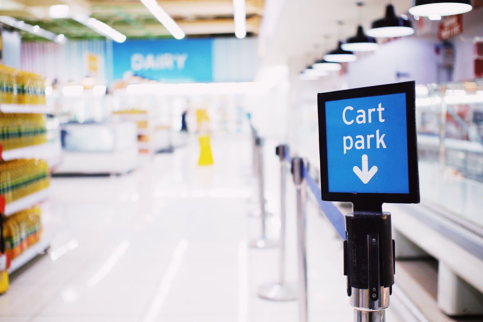 Interior de supermercado amplio y luminoso con un destacado cartel de 'Estacionamiento de Carritos' y pasillos vacíos.
