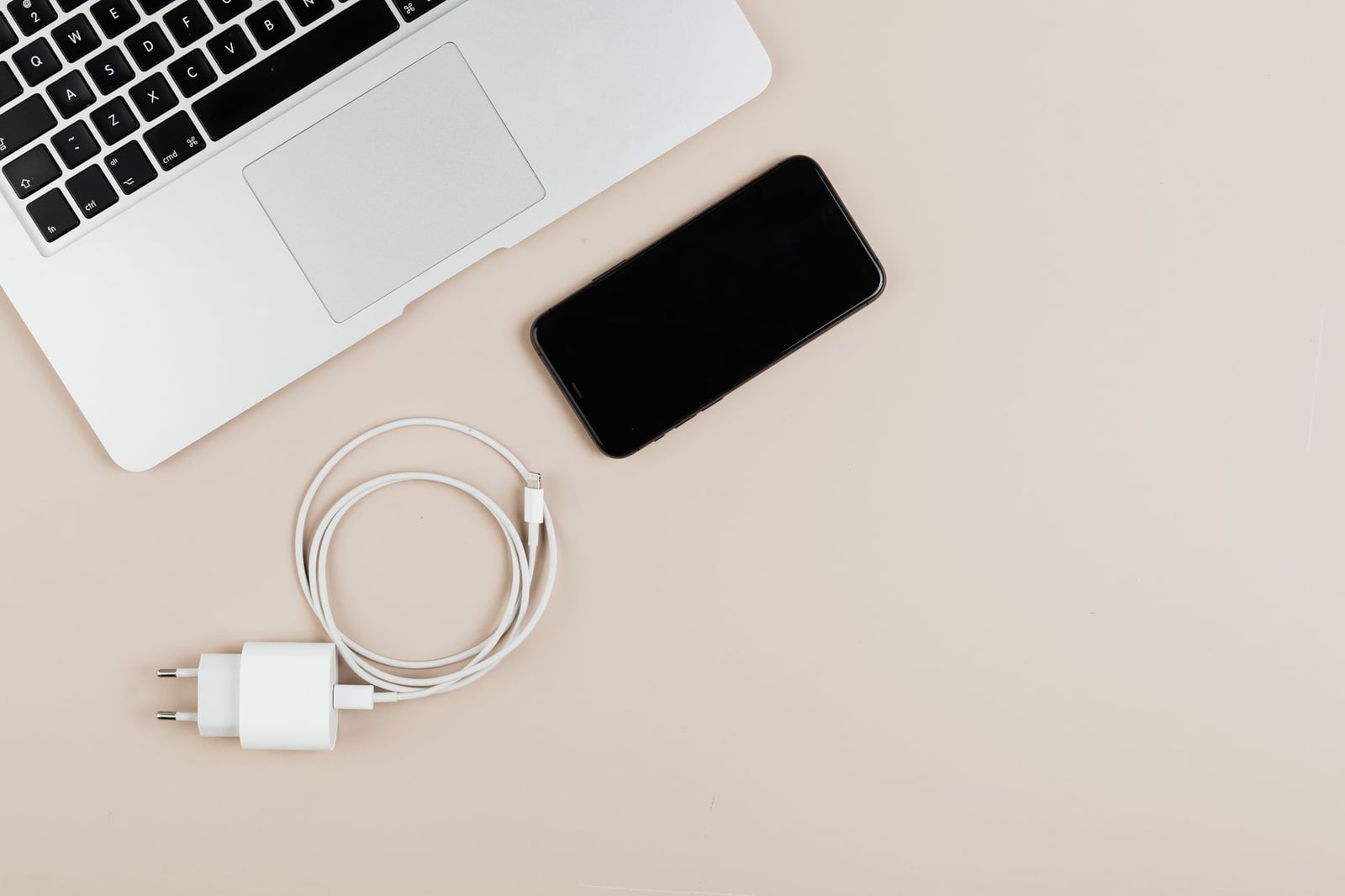 Vista plana de un portátil, teléfono inteligente y cargador sobre un fondo beige que muestra los elementos esenciales de la tecnología moderna.