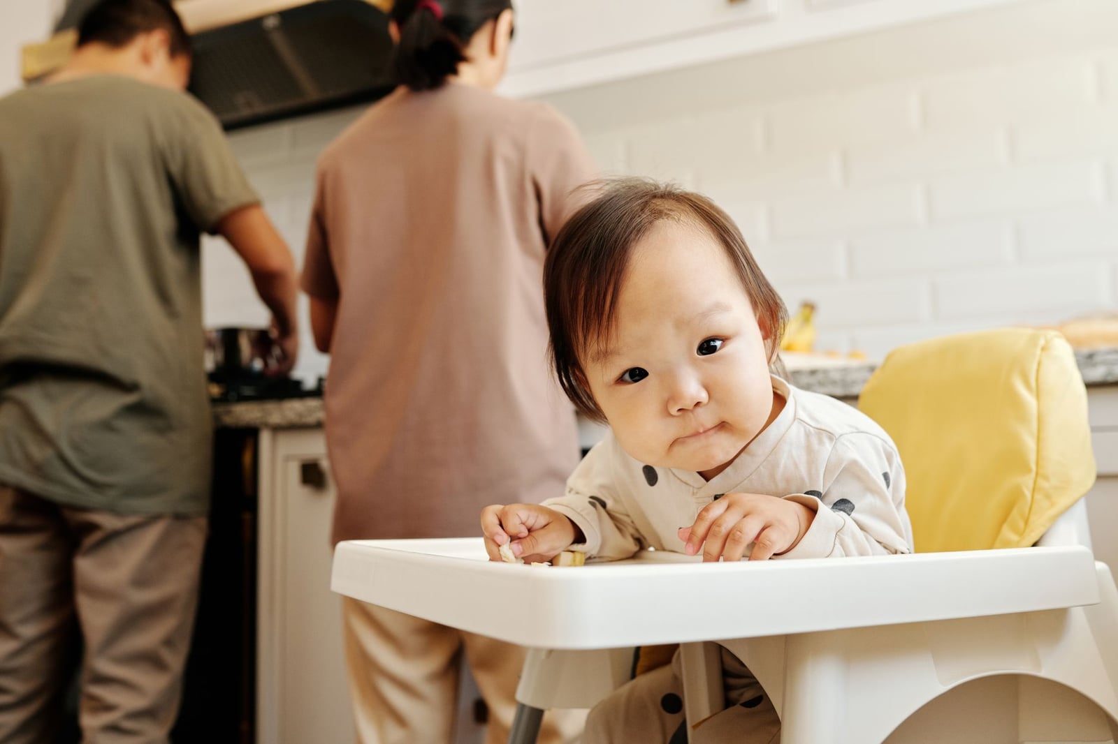 Niño lindo sentado en una silla alta mientras los padres preparan comida en la cocina.