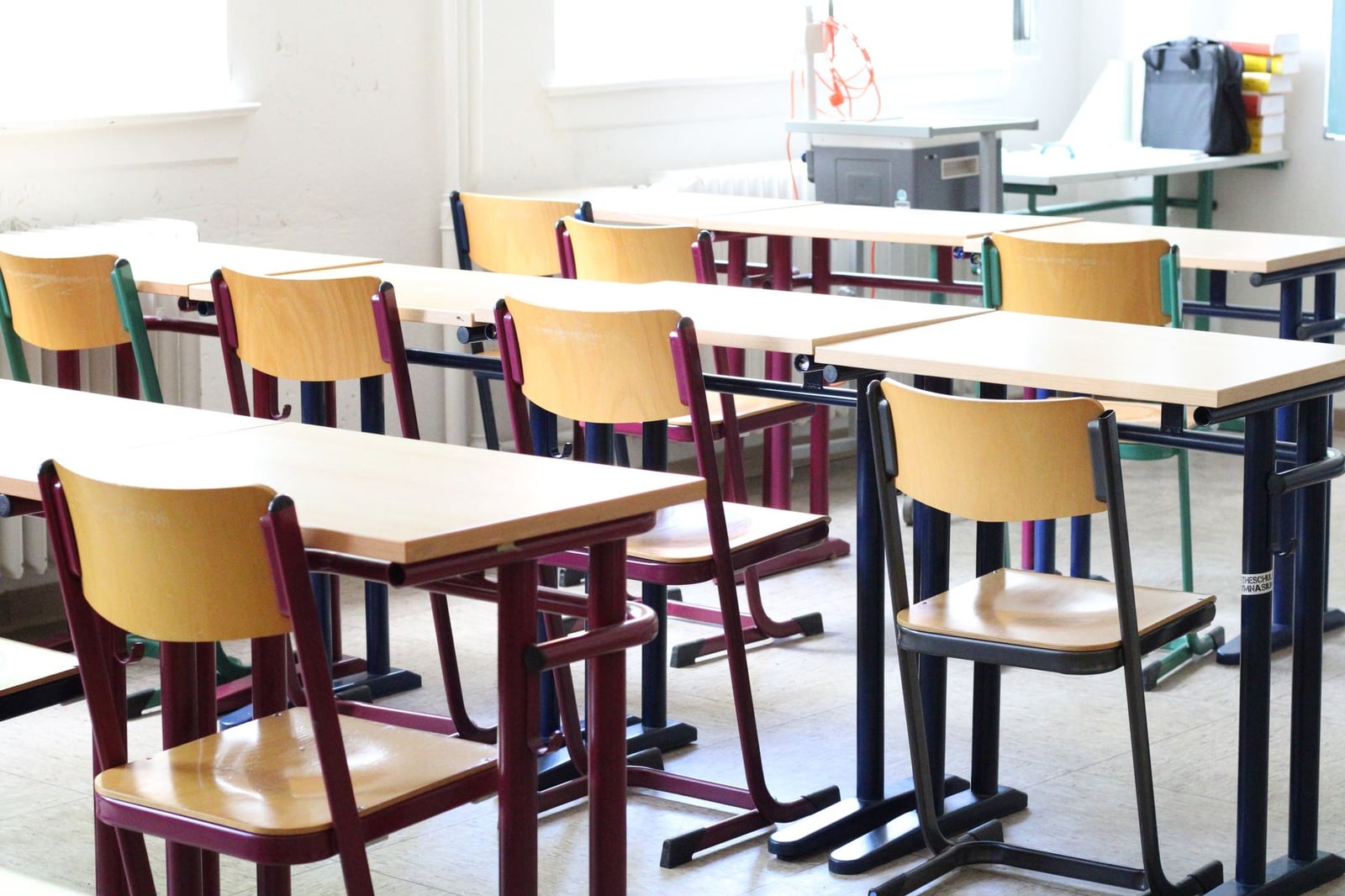 Un aula brillante y vacía con mesas y sillas de madera, lista para los estudiantes.