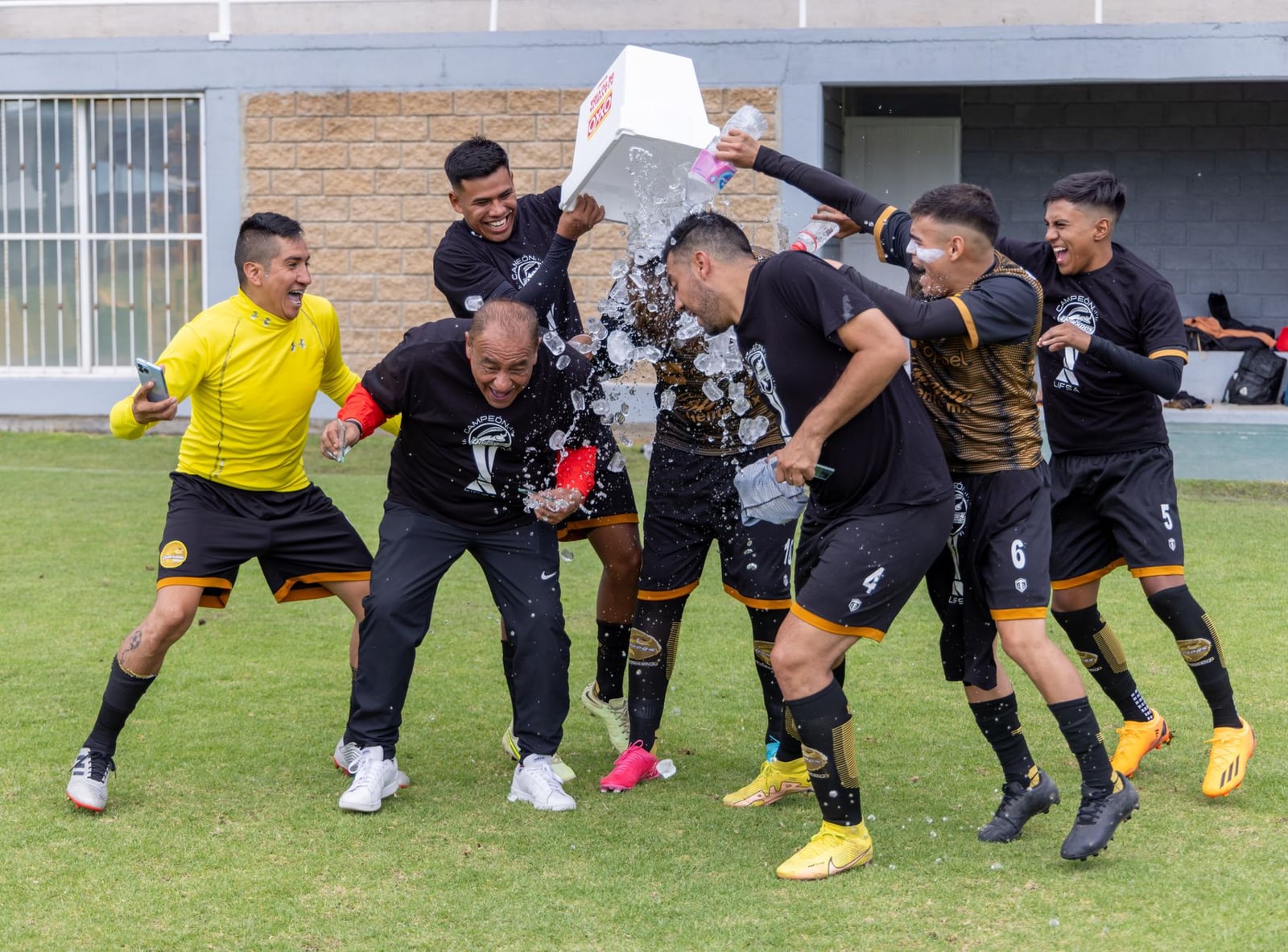 Equipo de fútbol celebrando la victoria con un alegre chapoteo de agua en el campo.