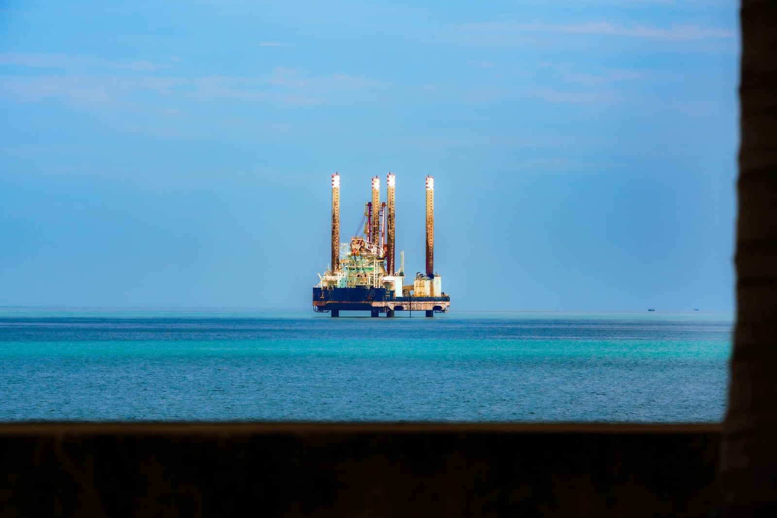 Vista lejana de una plataforma petrolífera en alta mar, en un océano azul y tranquilo, bajo un cielo despejado.