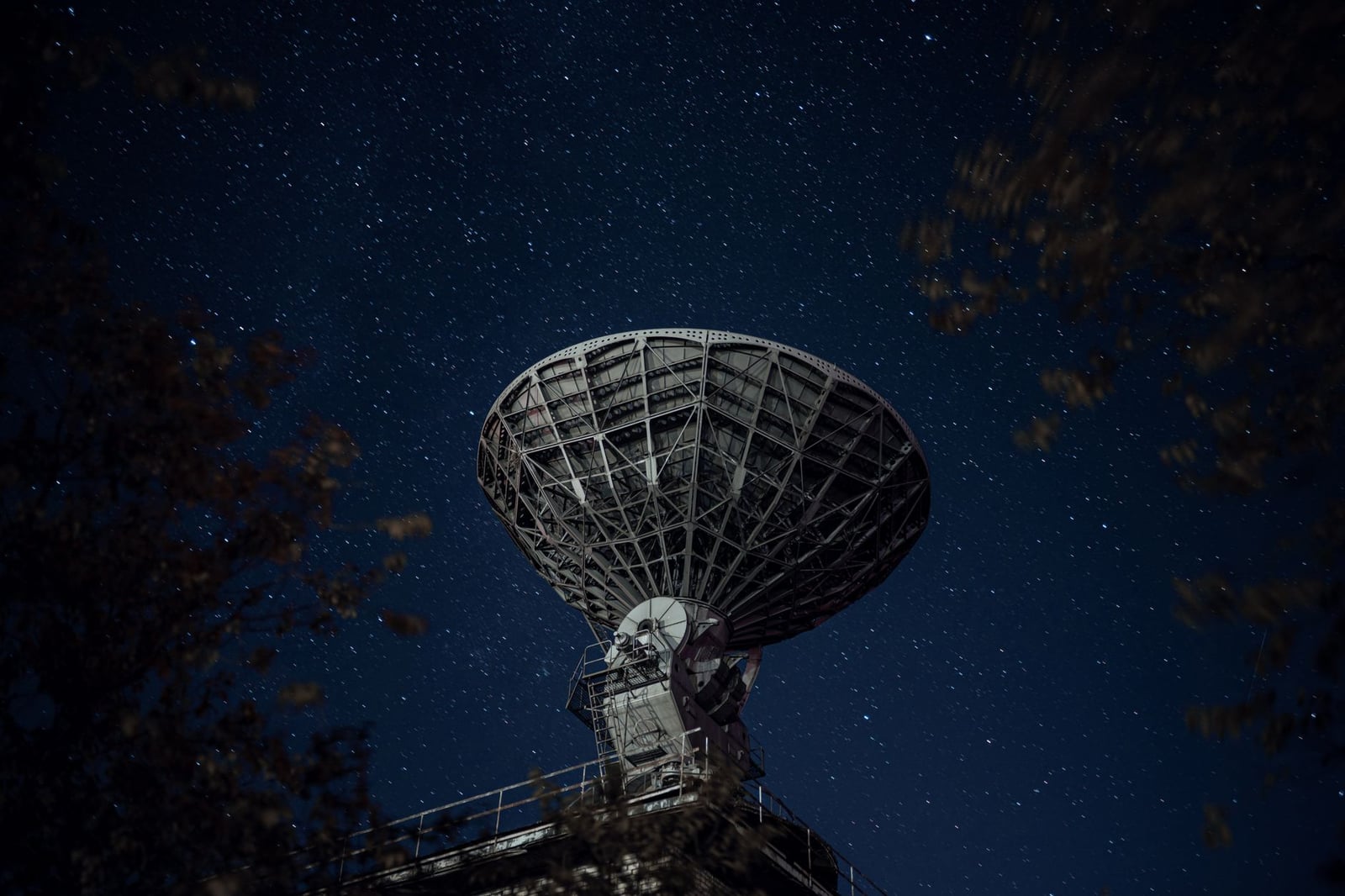 Un gran radiotelescopio bajo un cielo nocturno estrellado capturando señales celestiales.