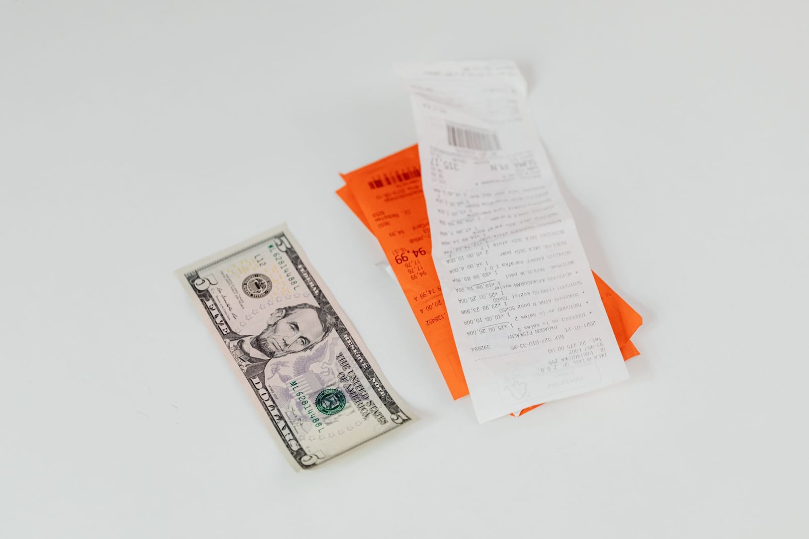 Primer plano de un billete de cinco dólares junto a recibos de compras sobre un fondo blanco, ideal para temas de finanzas y comercio.