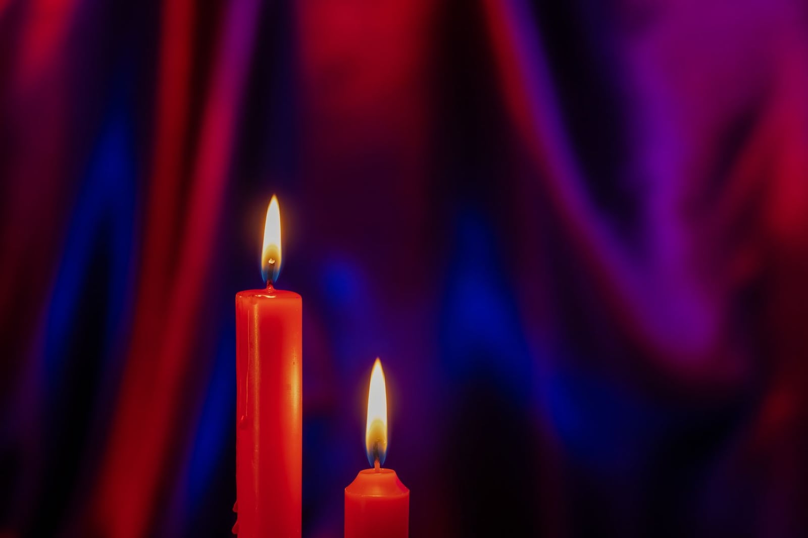 Velas rojas con llamas parpadeantes sobre un dramático fondo morado y rojo, creando una atmósfera cálida y melancólica.