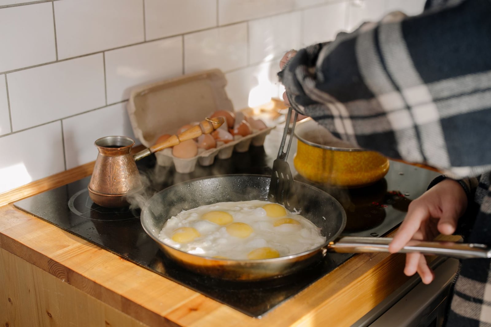 Primer plano de huevos cocinándose en la estufa con manos humanas en un entorno de cocina.
