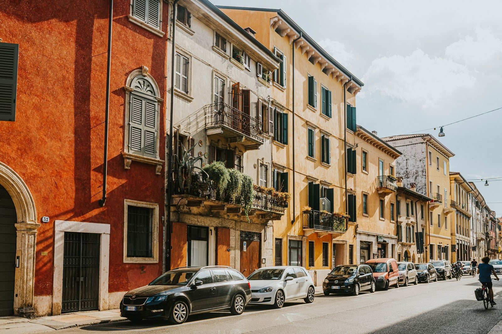 Edificios históricos coloridos y coches aparcados bordean las soleadas calles de Verona, Italia.