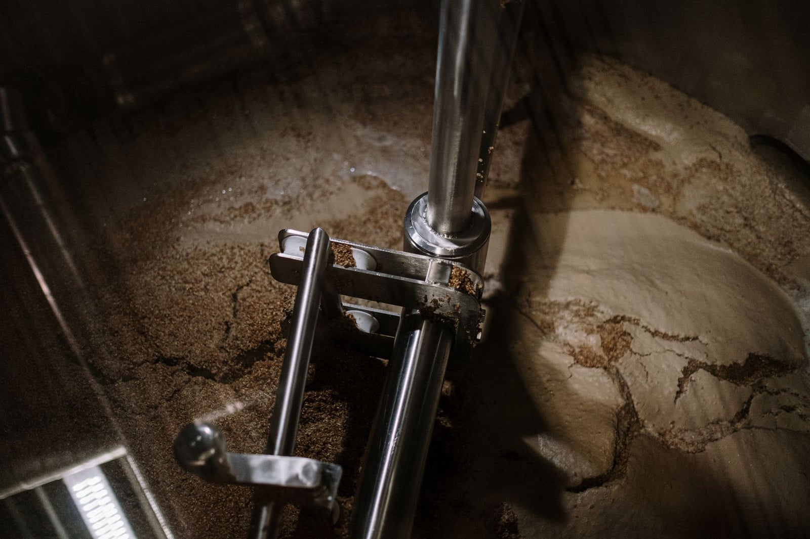 Primer plano de una mezcladora industrial de acero inoxidable removiendo el mosto de cerveza durante la fermentación en una cervecería.