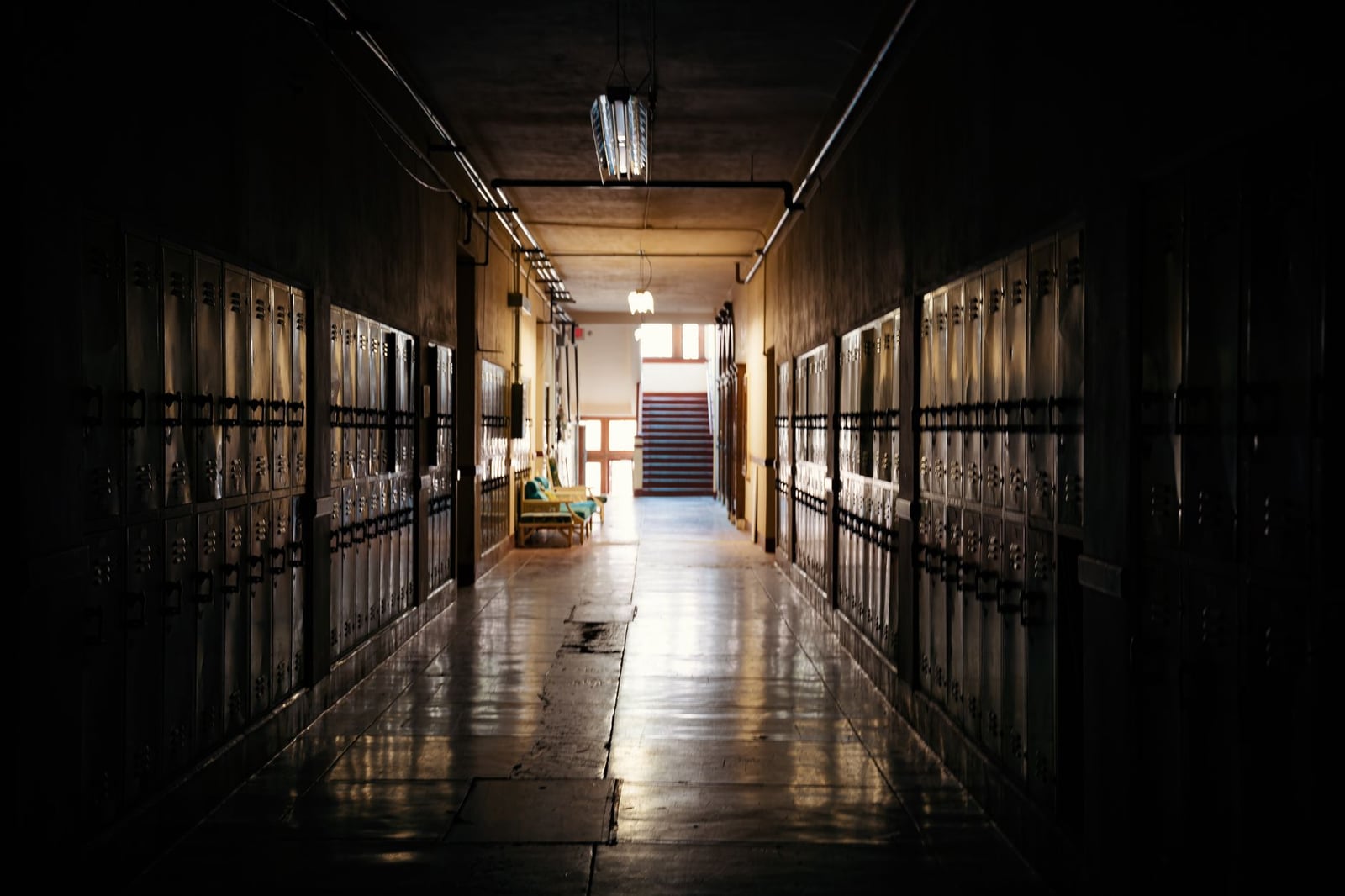 Un pasillo escolar oscuro y melancólico con casilleros y una fuente de luz a lo lejos.