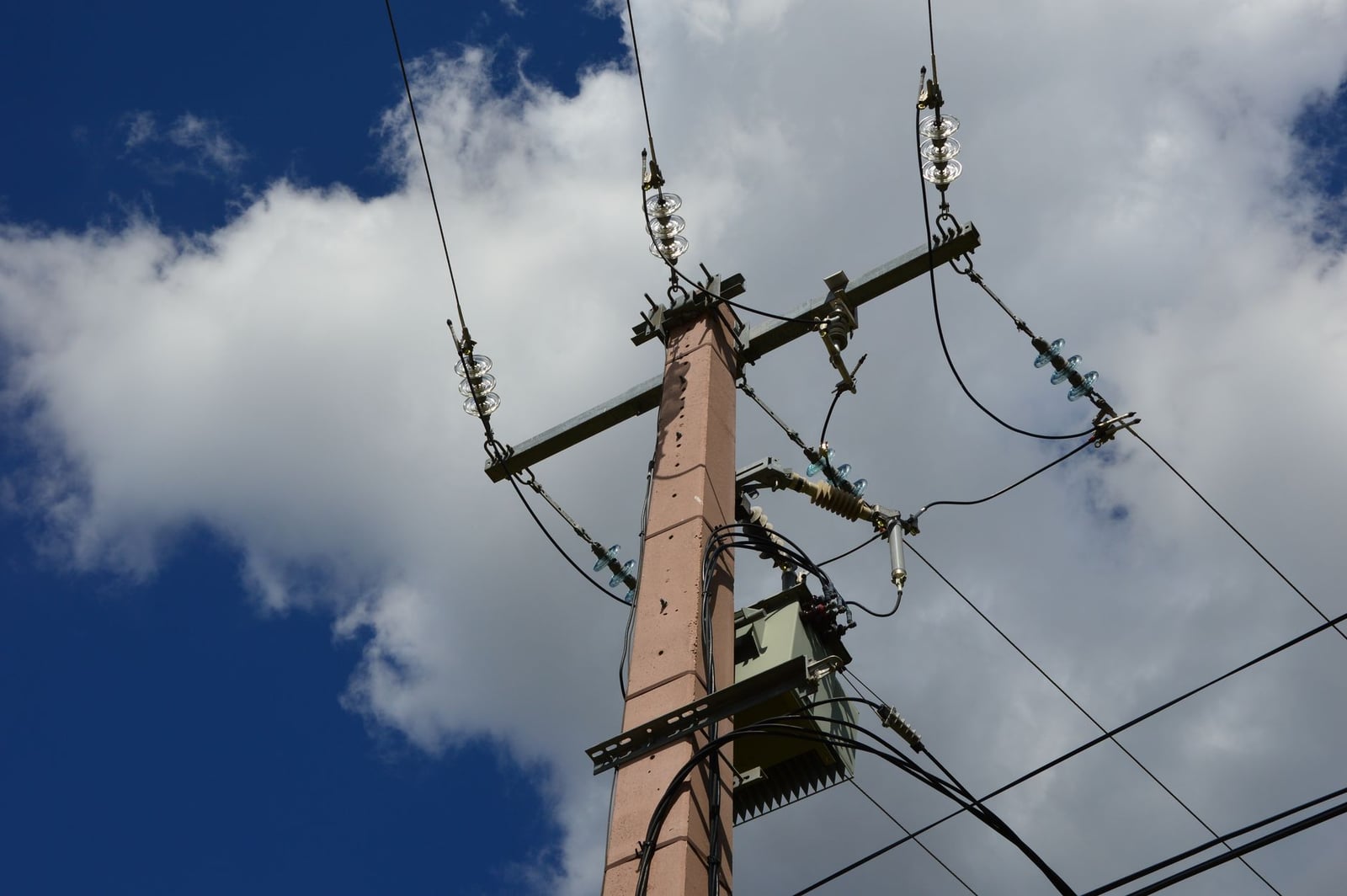 Vista en ángulo bajo de un poste de suministro y líneas eléctricas contra un cielo azul con nubes blancas.