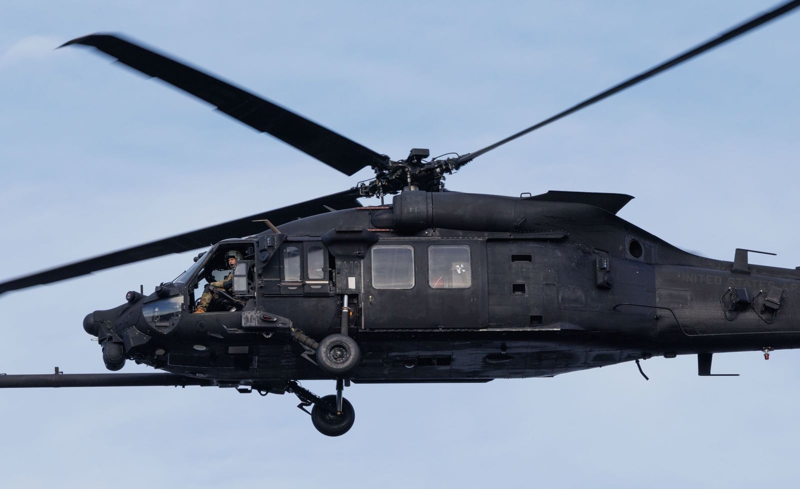 Un helicóptero militar negro volando en cielos azules claros, mostrando precisión en la aviación.