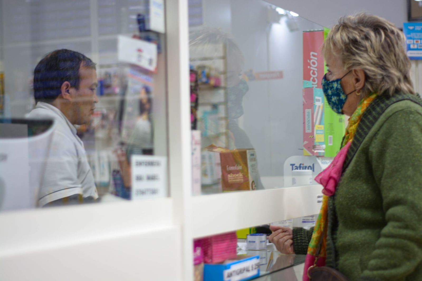 Una mujer con una máscara habla con un farmacéutico detrás del mostrador en una farmacia.