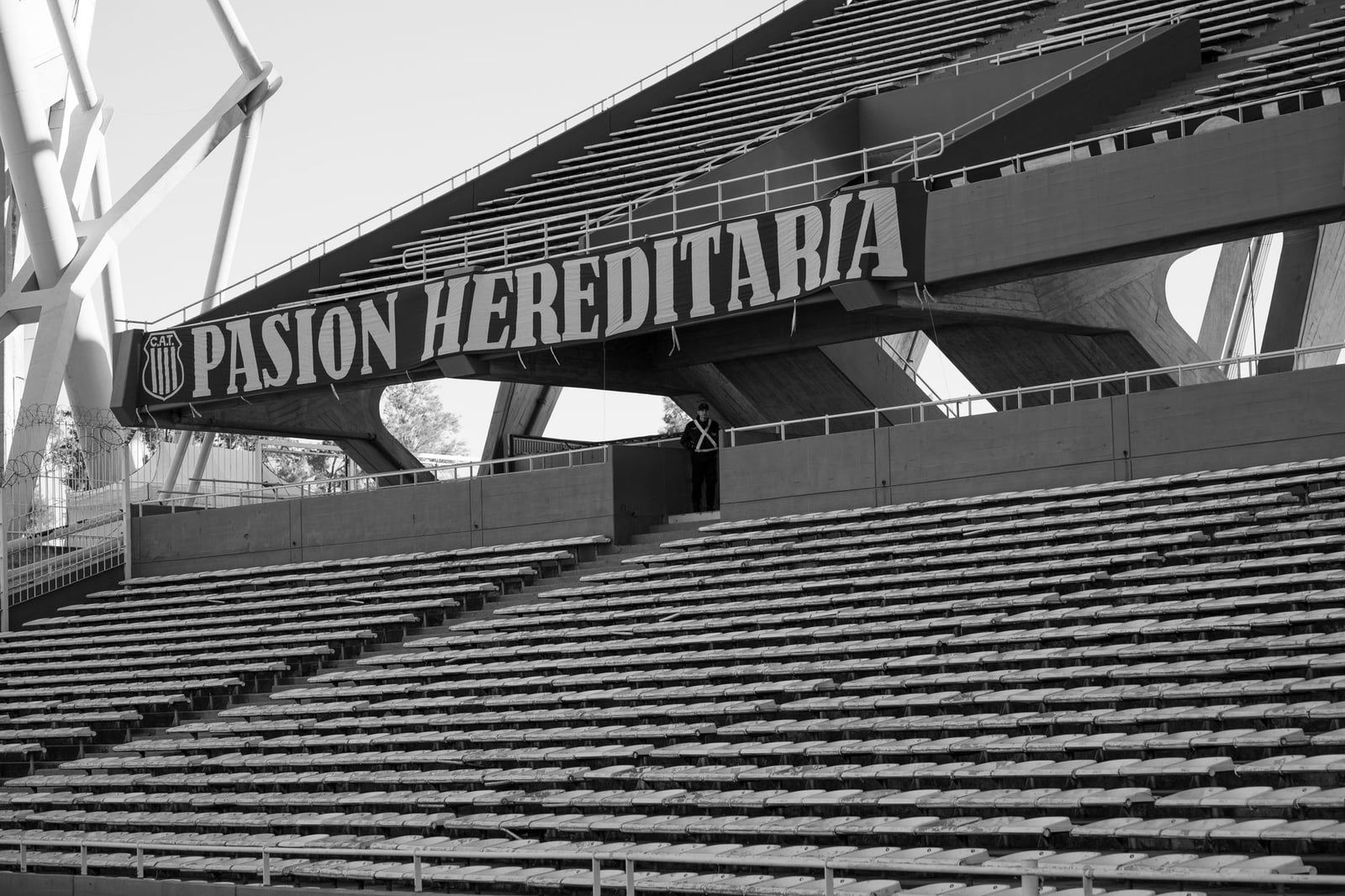 Fotografía en blanco y negro de las tribunas vacías de un estadio de Córdoba, resaltando la estructura y la atmósfera.