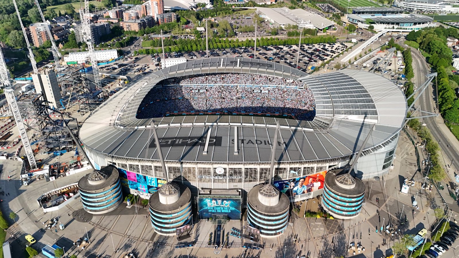 Toma de drone de un Estadio Etihad abarrotado en Manchester, Inglaterra, mostrando un paisaje urbano vibrante.