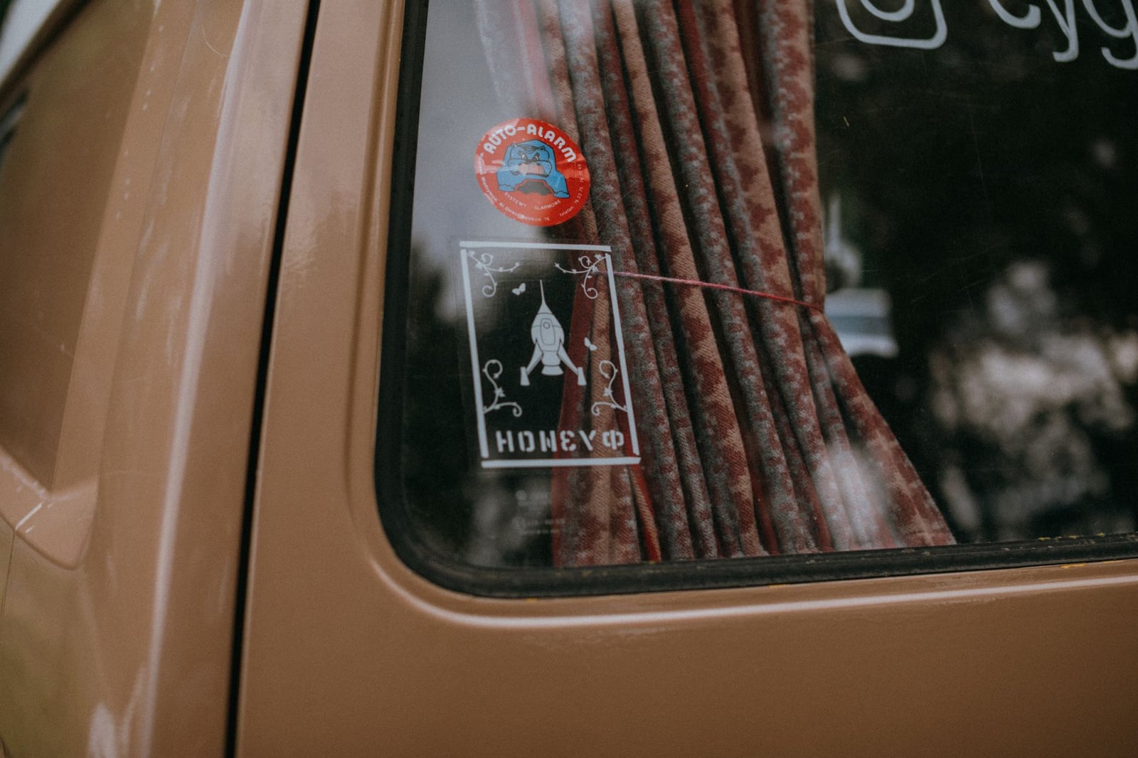 Acercamiento a la ventana de un coche vintage adornada con calcomanías de cohetes y cortinas.