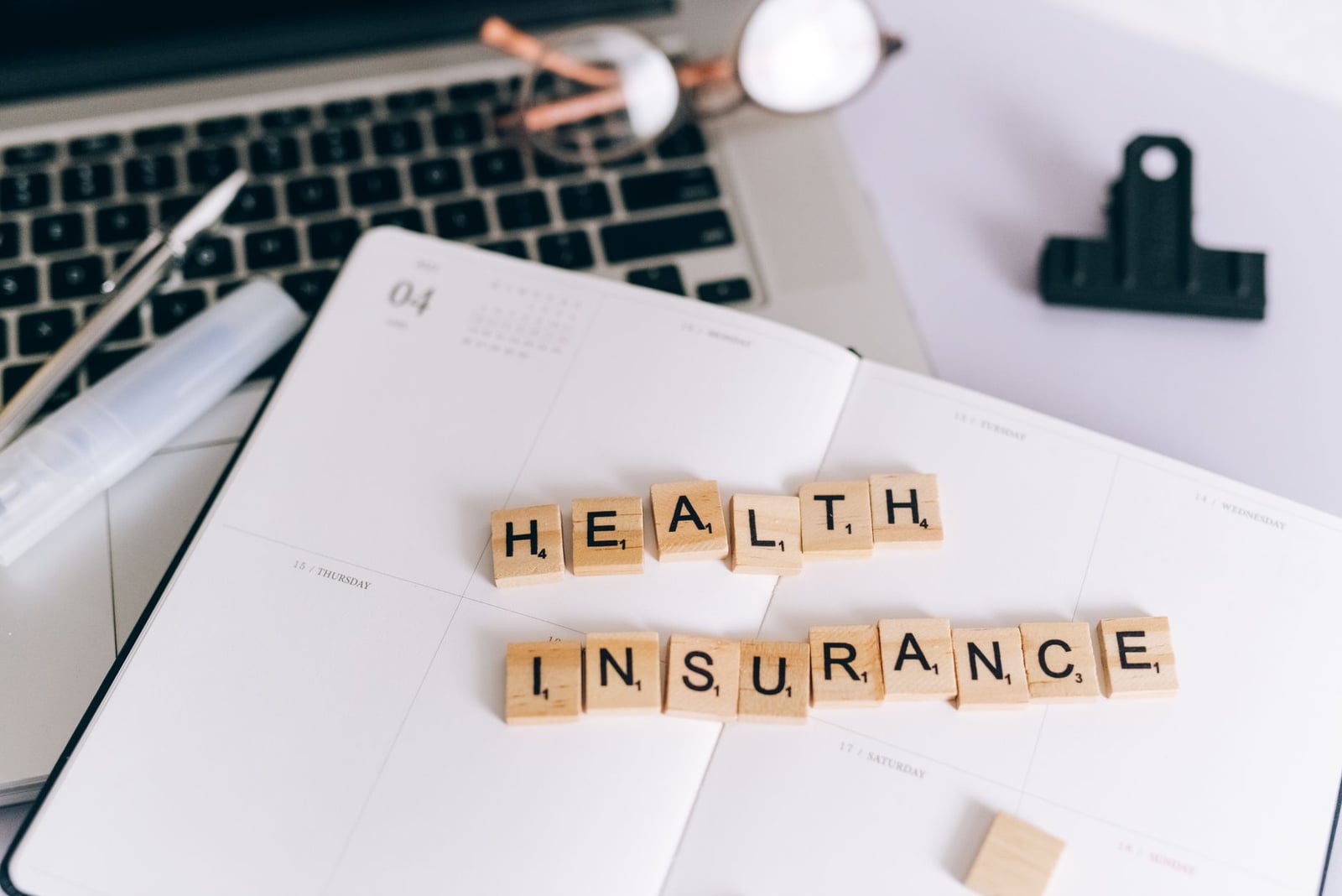 Primer plano de letras de Scrabble que dicen 'Seguro de Salud' en una agenda con un laptop.