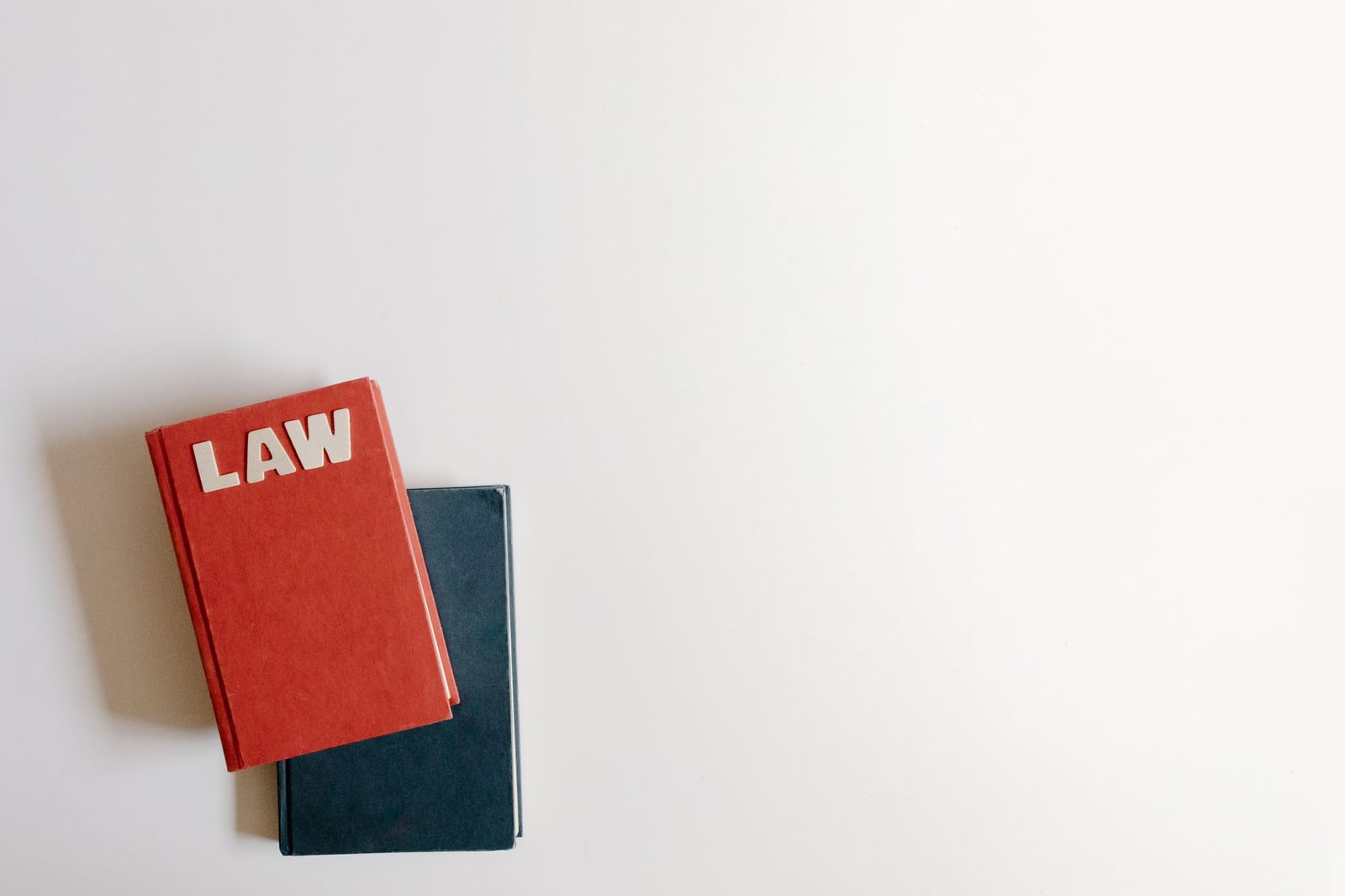 Planos de un libro de derecho rojo y un libro azul sobre un fondo blanco, perfecto para temas legales.