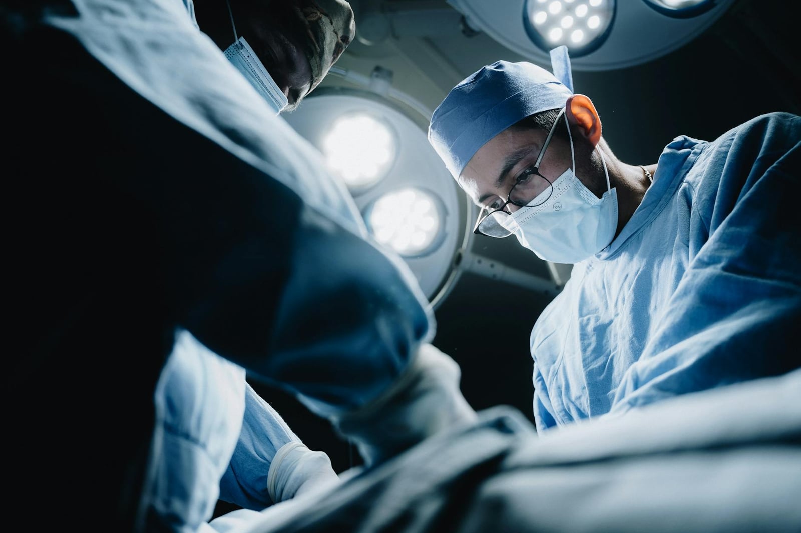 Médicos con uniforme quirúrgico se concentran en una operación bajo luces brillantes en un quirófano moderno.