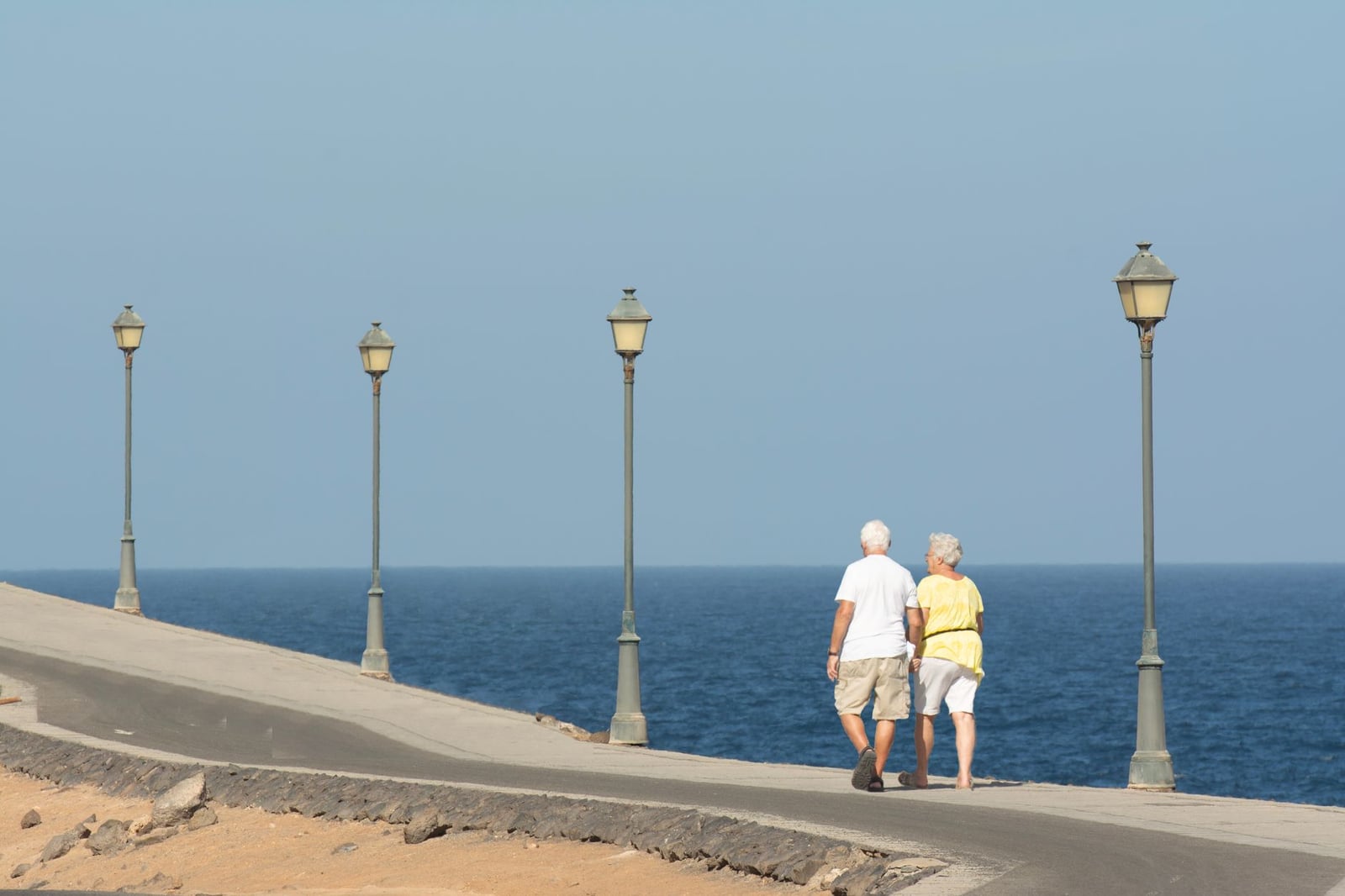 Pareja mayor caminando por un paseo marítimo disfrutando de un día tranquilo junto al mar.