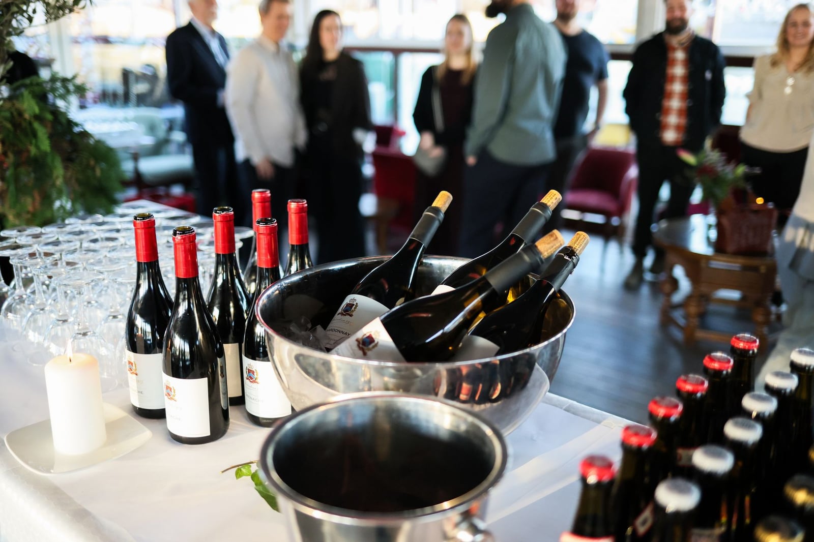 Reunión exclusiva con botellas de vino y gente mezclándose en el interior, creando un ambiente sofisticado.